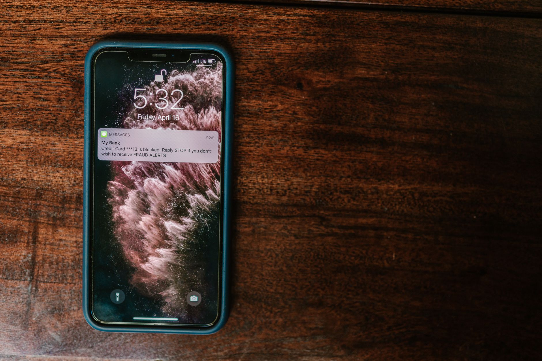 Close-up of smartphone on wooden surface displaying a bank alert message.