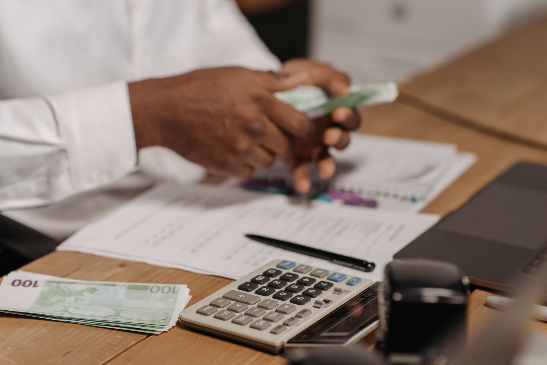 Hands counting euro bills on a wooden desk with calculator, financial documents,