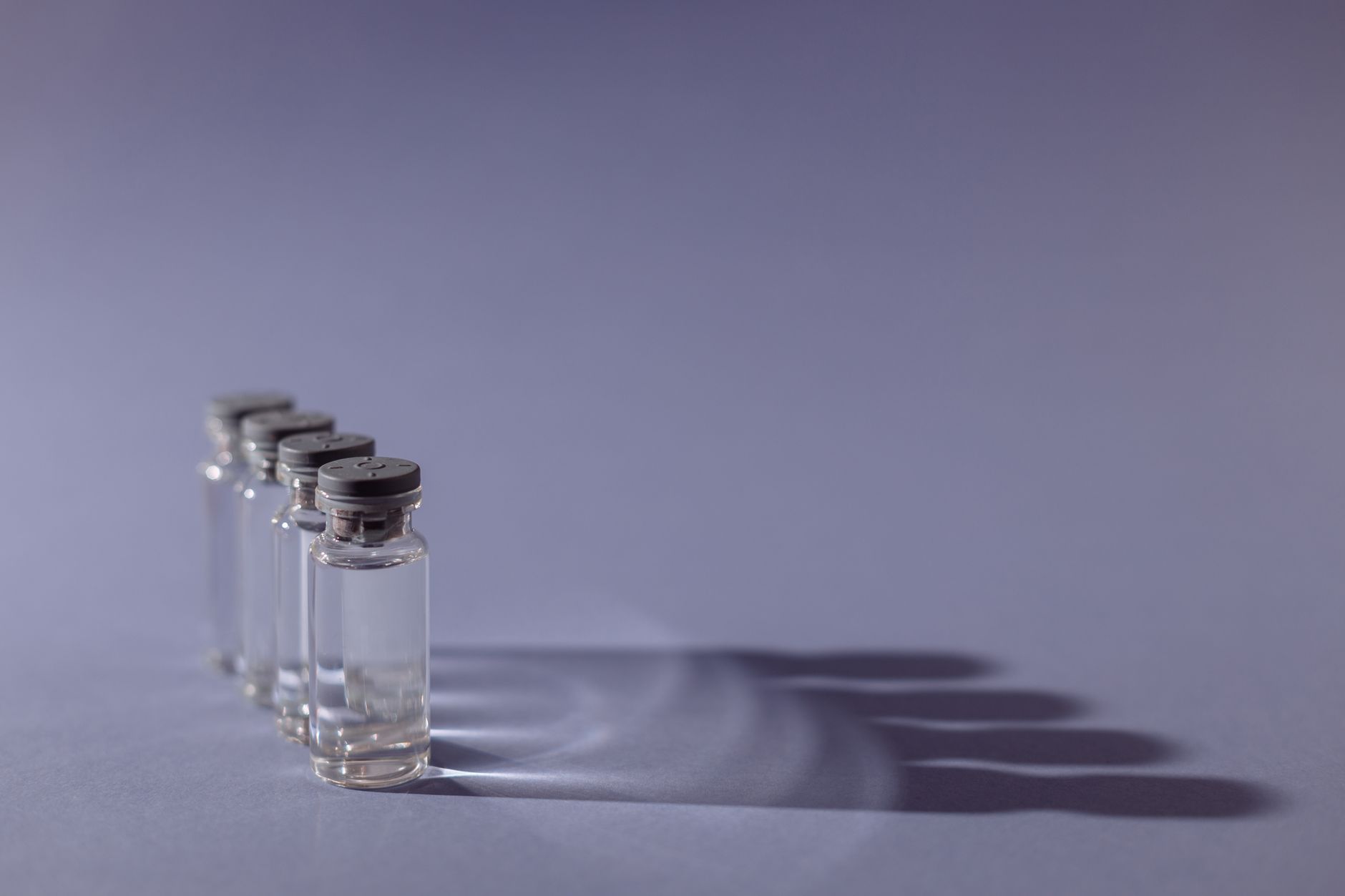 Close-up of lined up vaccine vials casting shadows, symbolizing medical advancements and