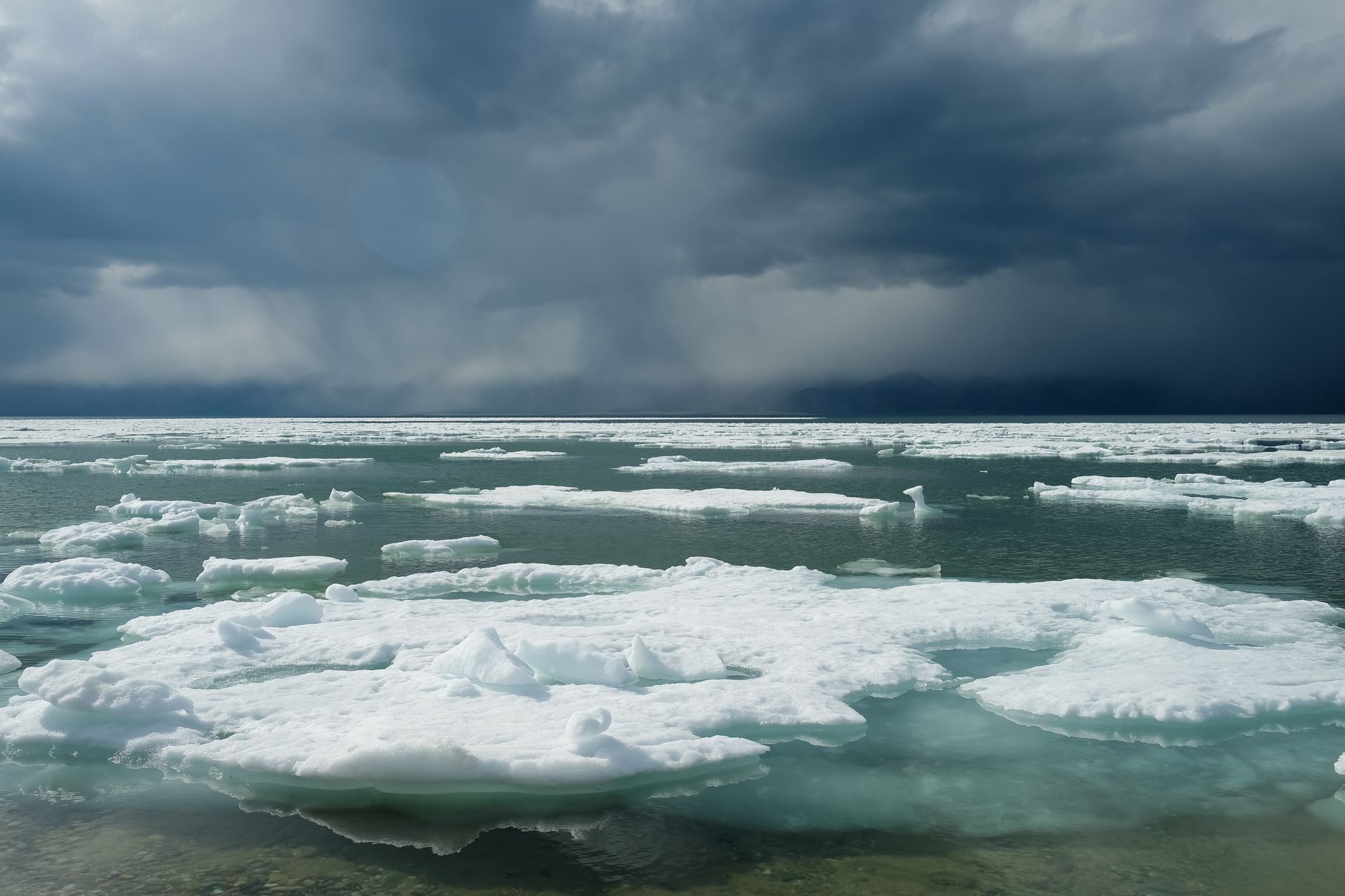 A moody seascape with floating sea ice against dark clouds in Russia.