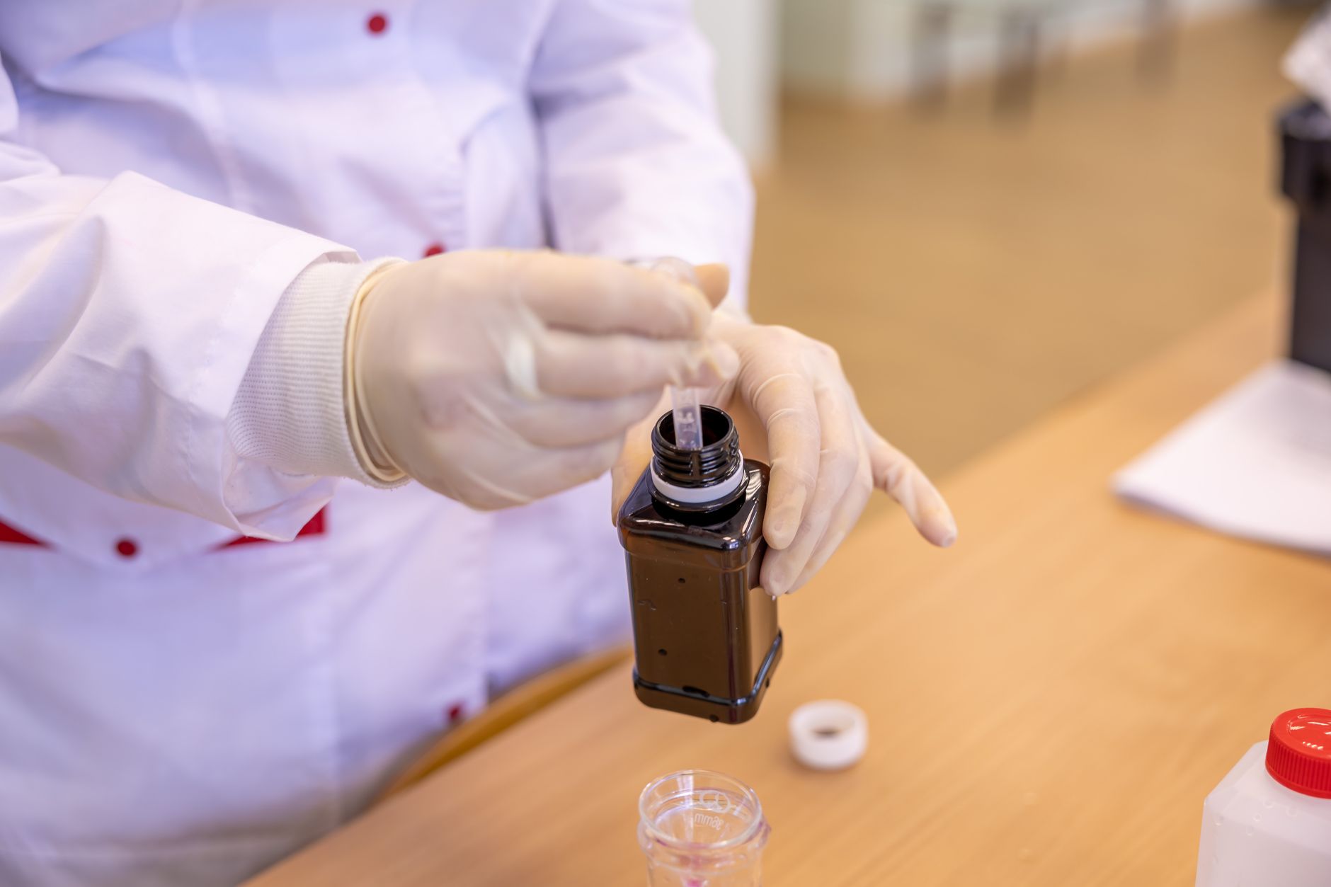 Scientist in protective gear extracting liquid sample from a bottle in a