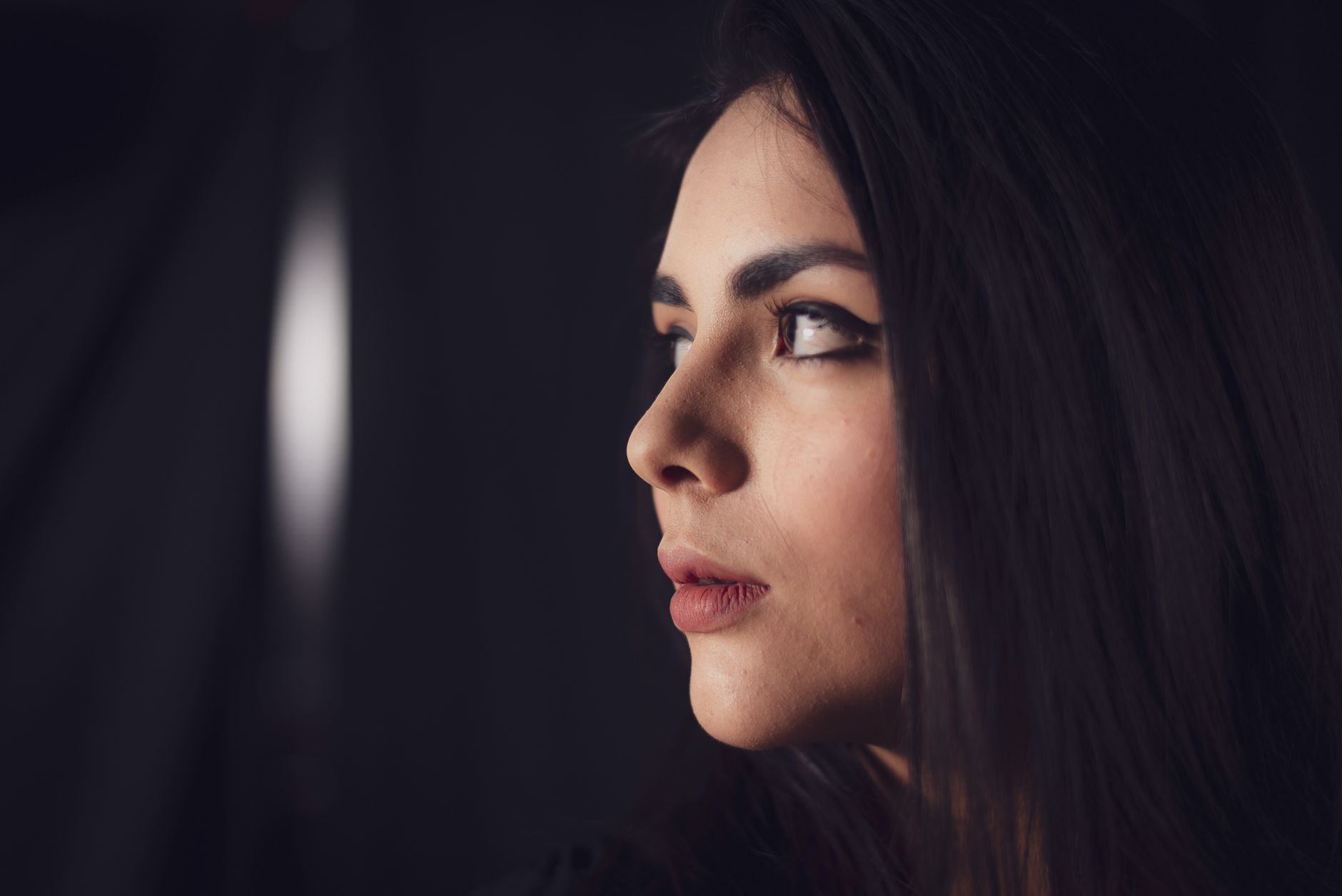 Close-up side profile of a woman with elegant makeup against a dark
