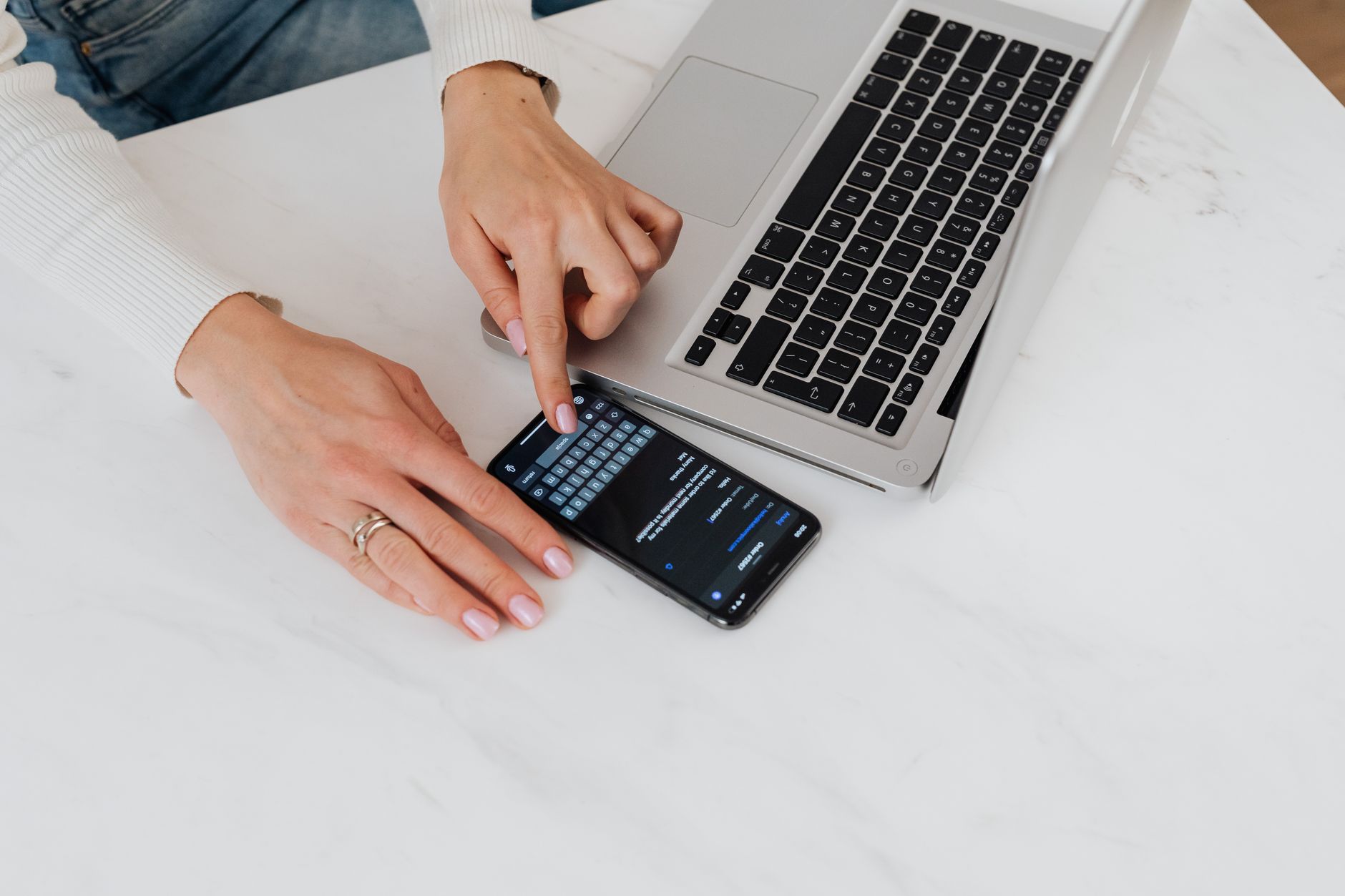 Close-up of hands using smartphone and laptop on a white desk. Perfect