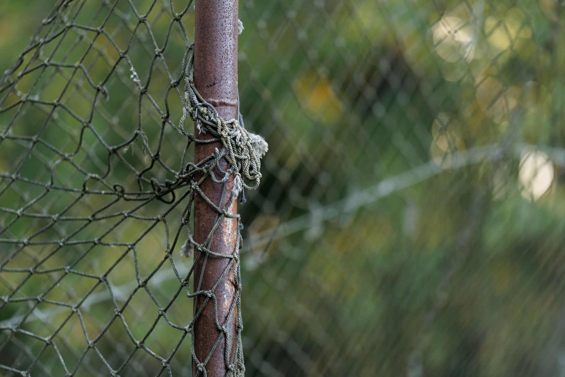 Close-up of a weathered chain-link fence tied to a rusty pole with
