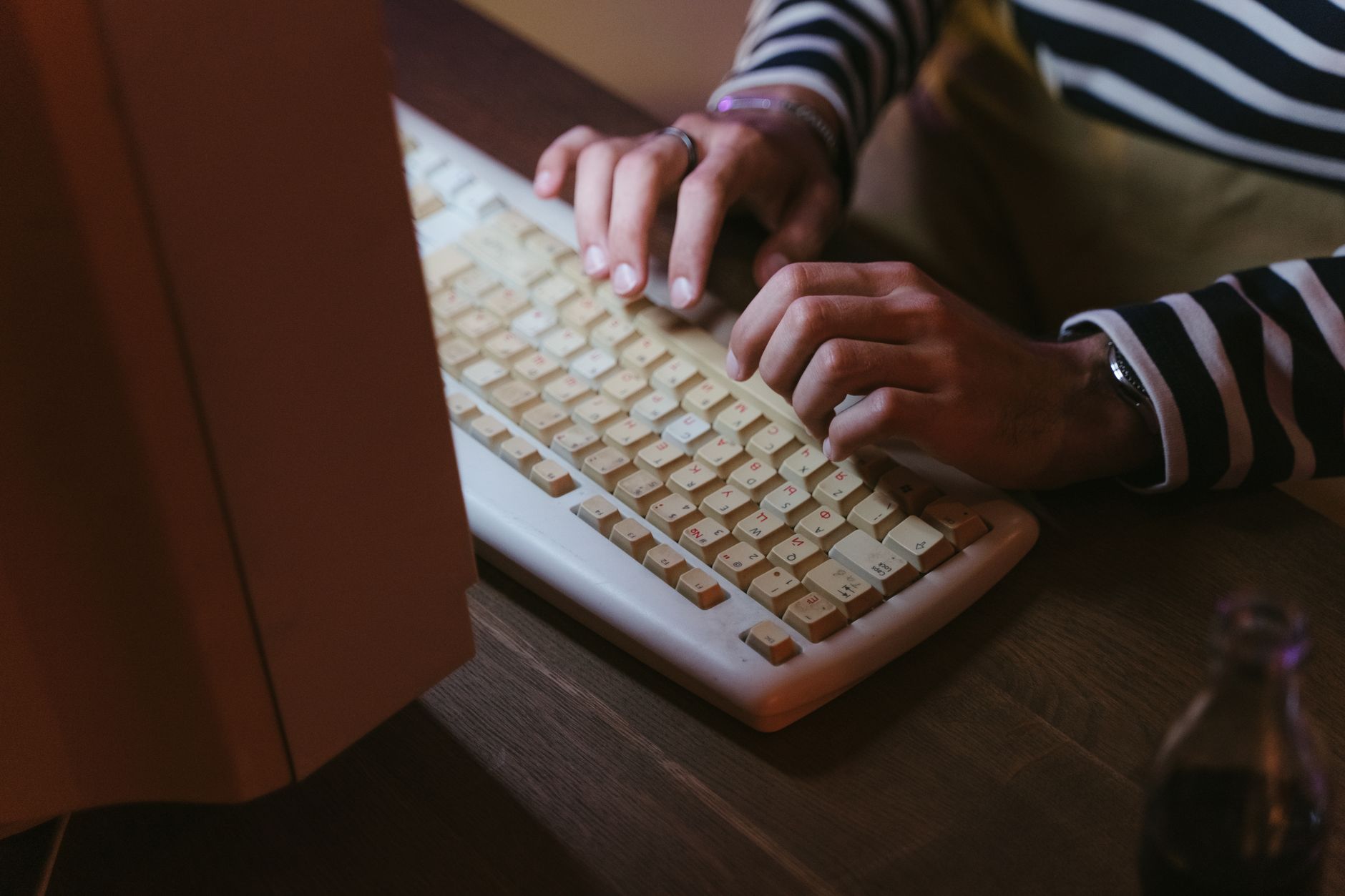 Hands typing on a vintage beige keyboard with a striped sweater visible,
