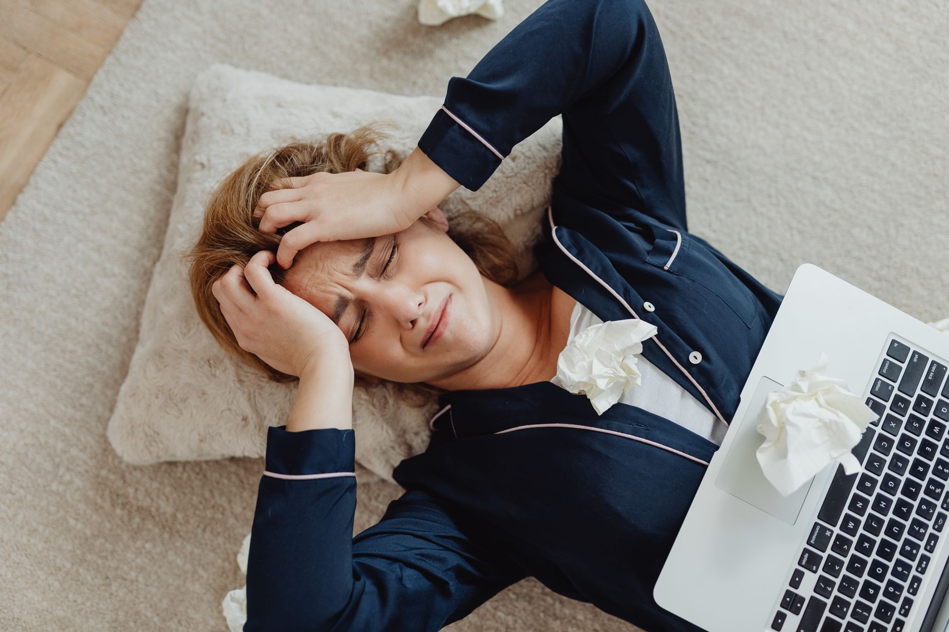 Overhead view of a frustrated woman in loungewear with a laptop and crumpled papers, facing remote work stress.
