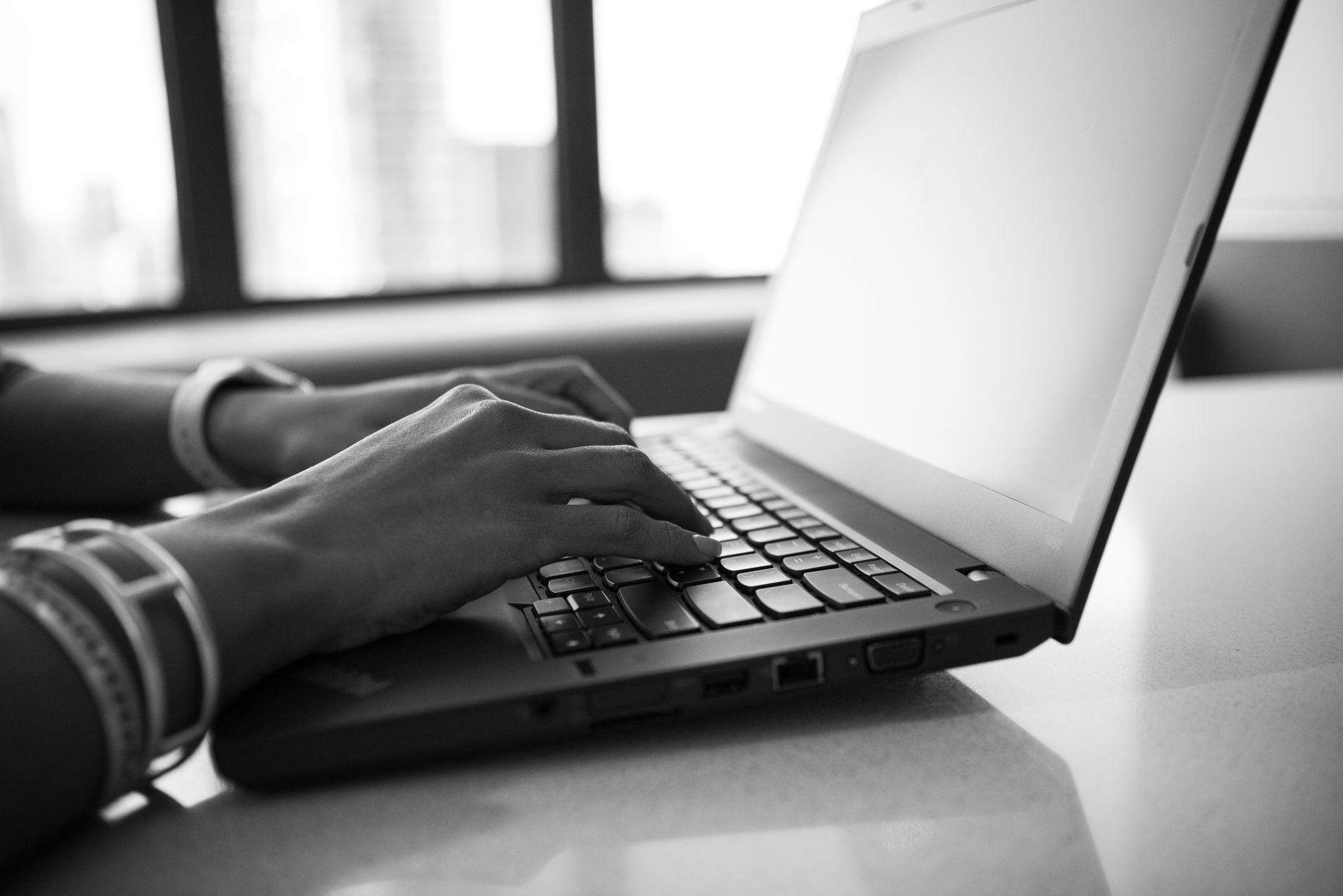 Close-up black and white photo showing hands typing on a laptop, emphasizing