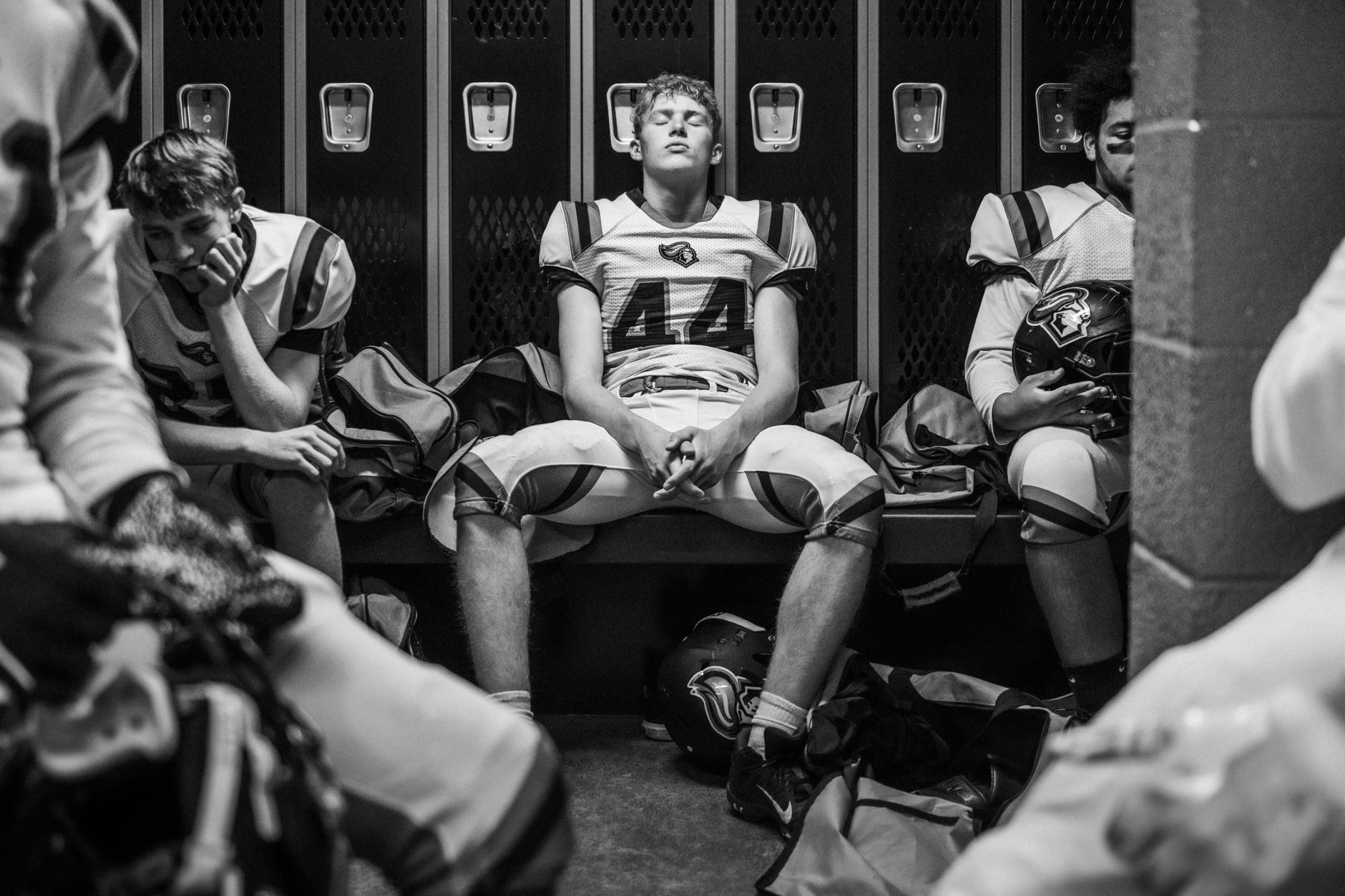 Black and white image of high school football players reflecting in locker