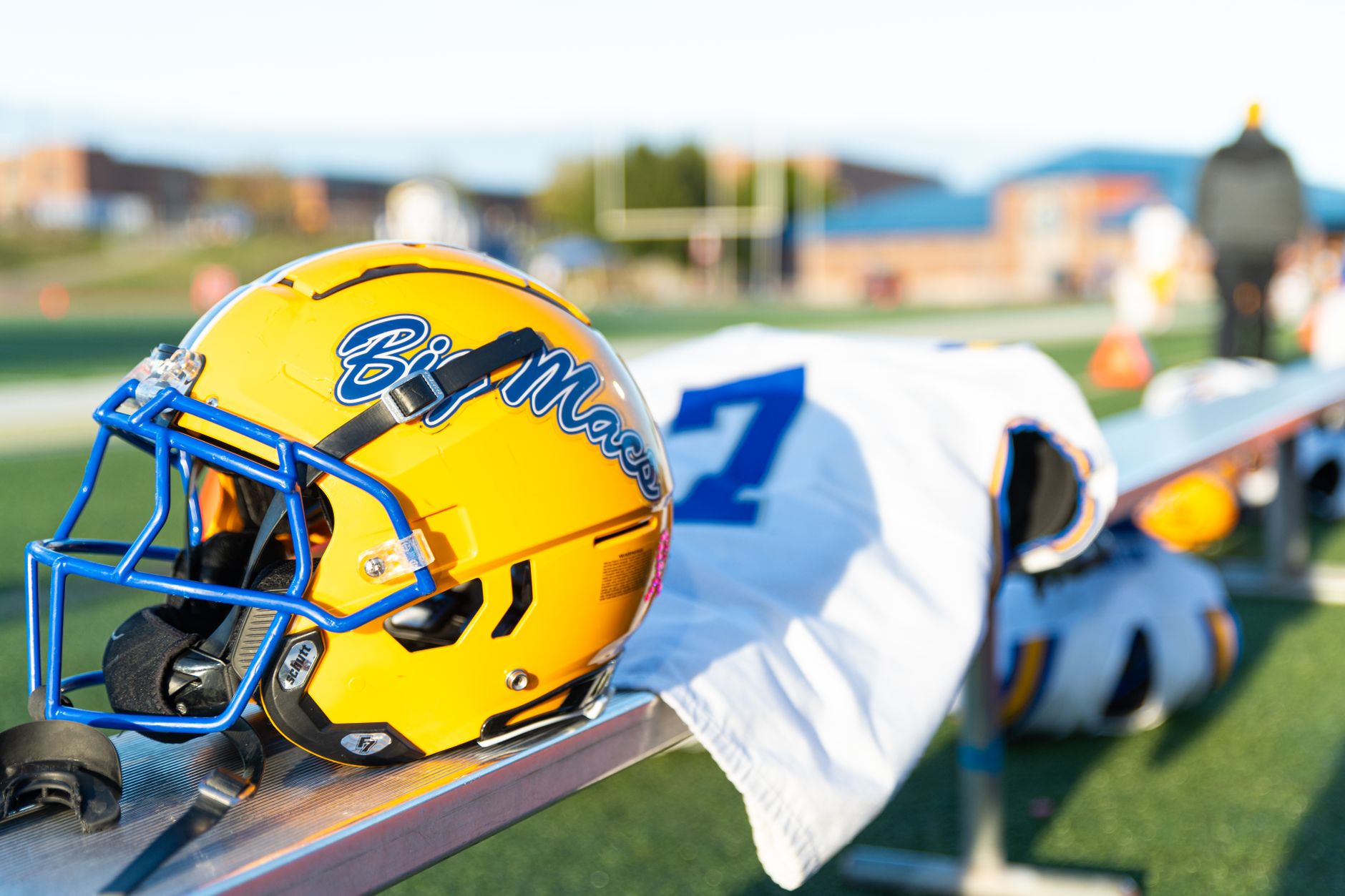 A yellow football helmet with blue highlights rests on a sports bench,