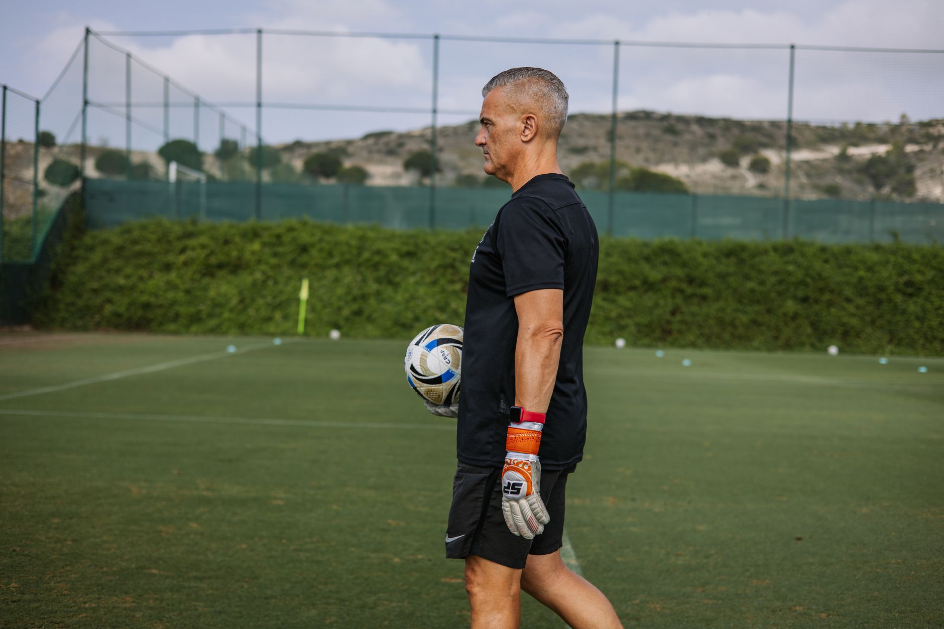 Experienced coach holding a soccer ball during football practice outdoors.