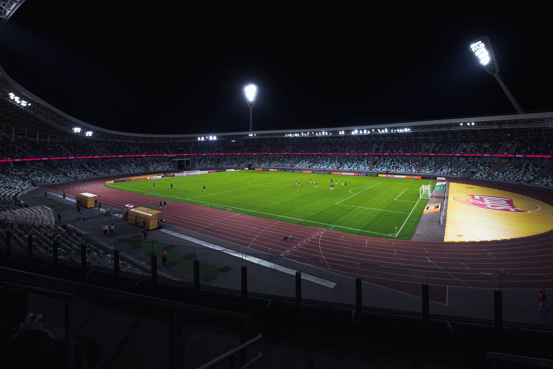 Brightly lit empty soccer stadium with green field under spotlights during night
