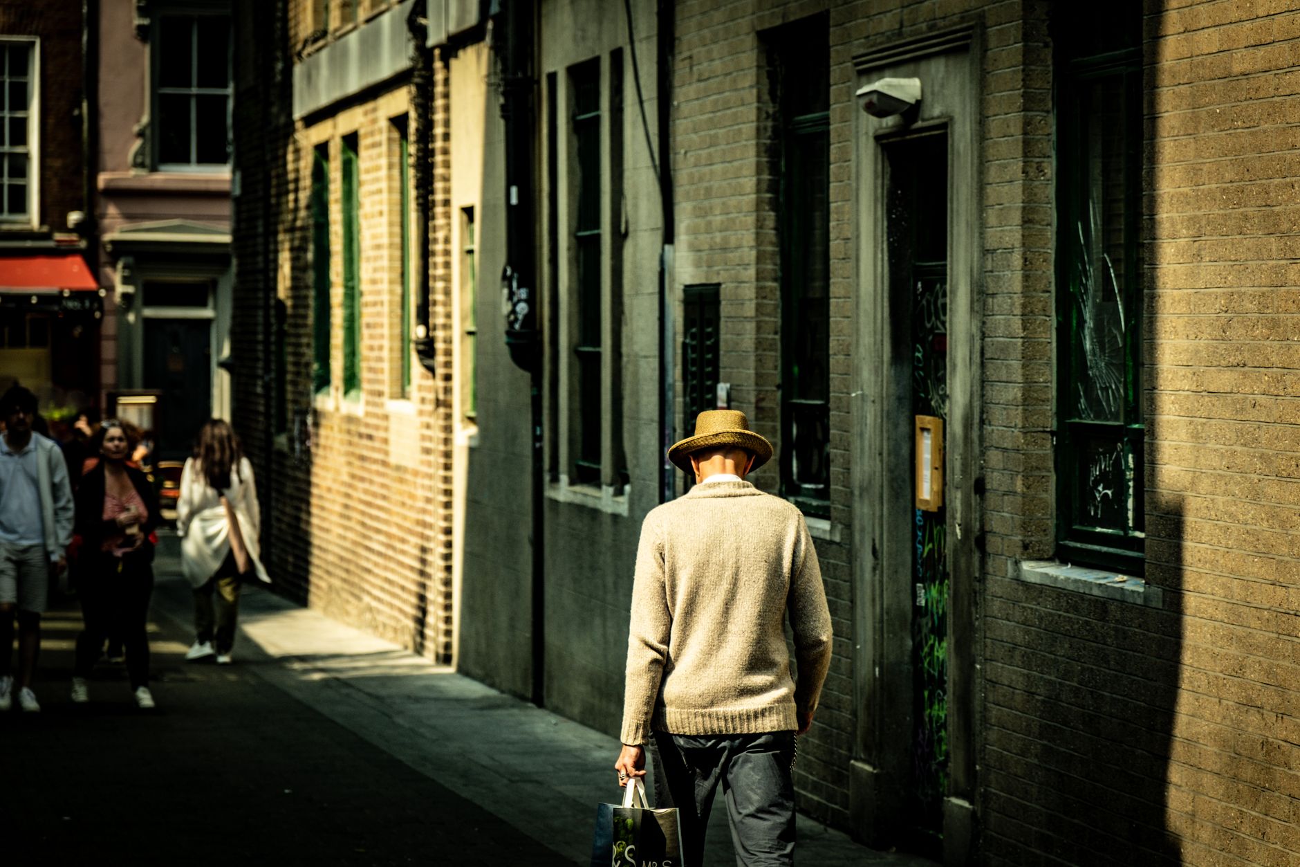 A man with a hat walks down a sunlit alleyway in Dublin, Ireland, capturing the play of light and shadow.
