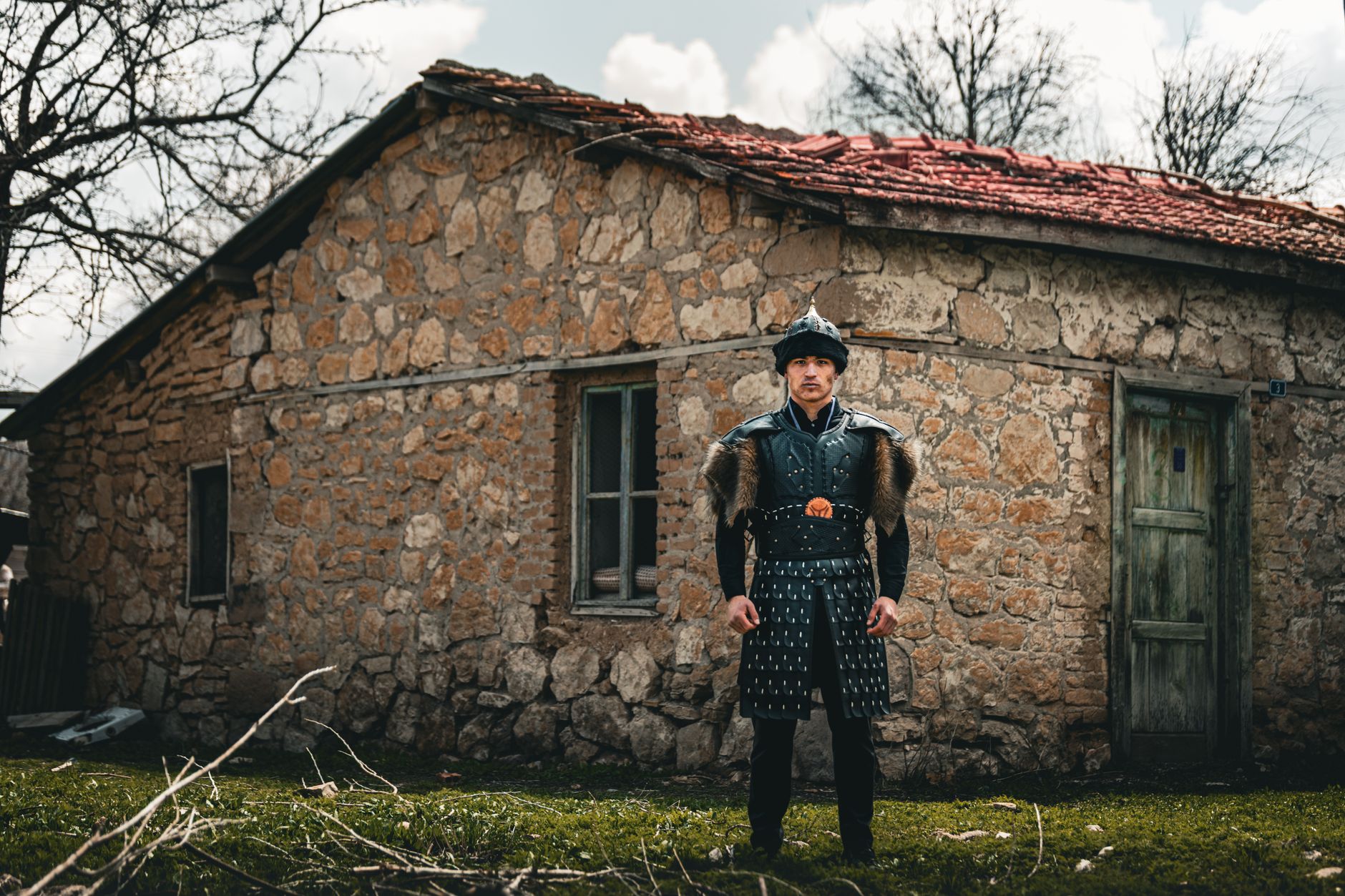 A medieval warrior in armor stands in front of a rustic stone