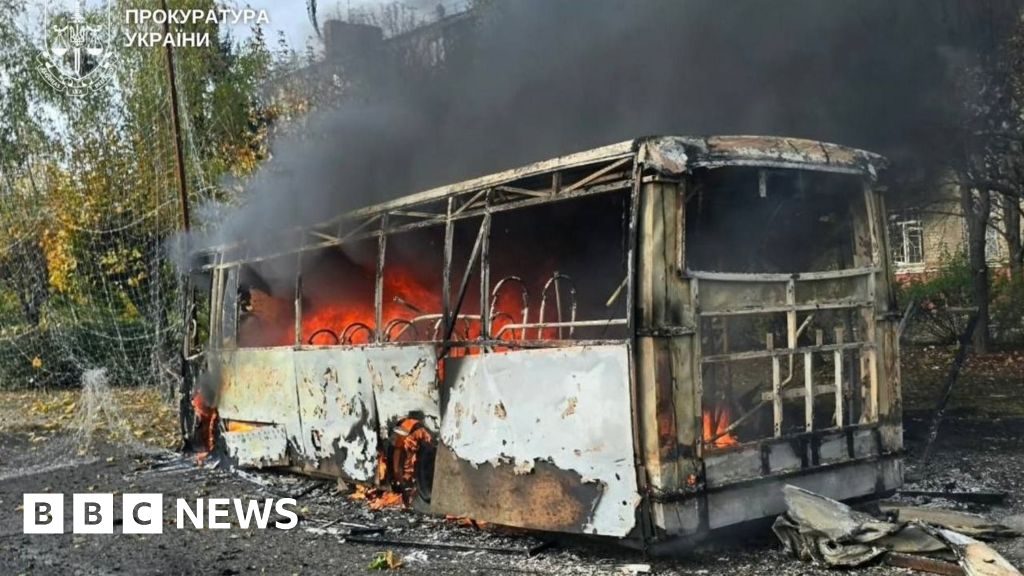 The burning metal shell of a bus in Kramatorsk. Flames can be seen inside the bus with black smoke coming out, with debris strewn across the road