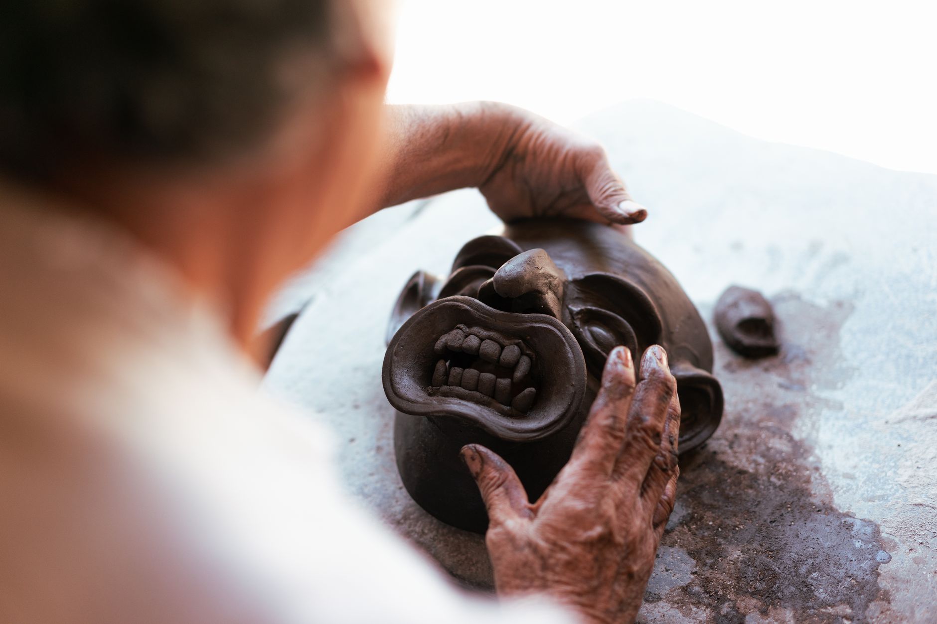 Close-up of an artisan crafting a clay mask with detailed hands-on technique.