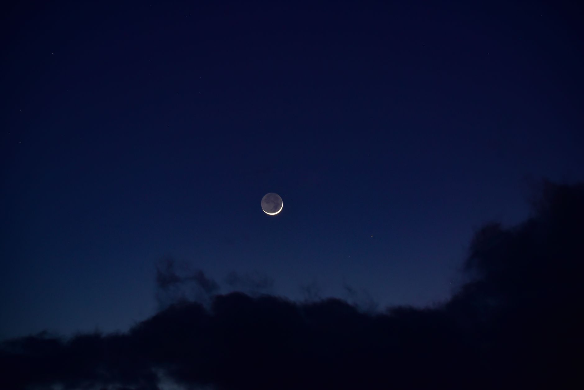 A serene crescent moon surrounded by deep blue night sky and fluffy
