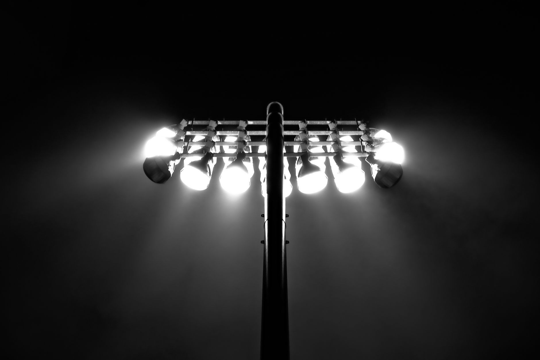 Black and white photo of stadium floodlights illuminating the night sky in