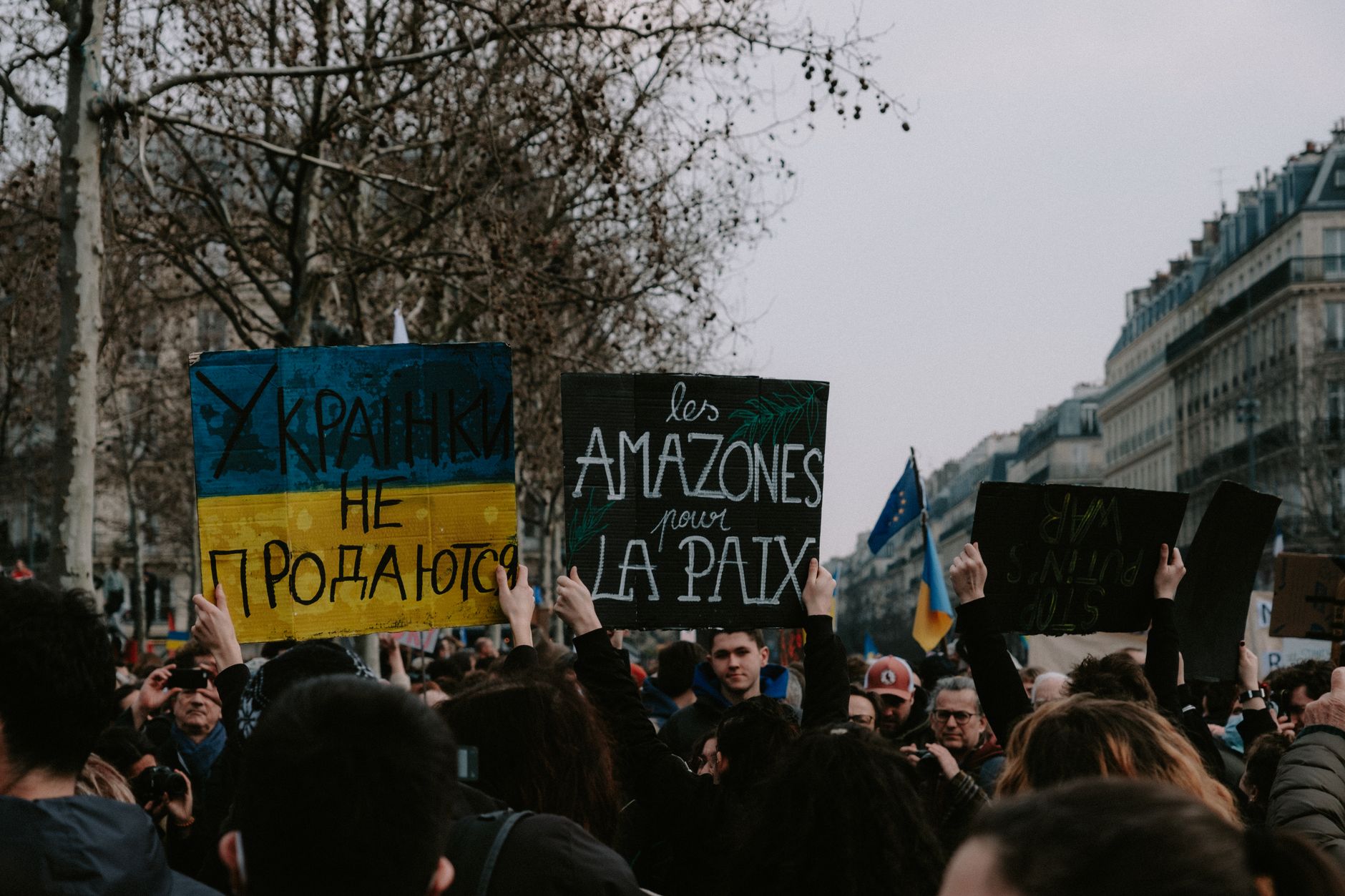 A large group of people rally in the street holding diverse protest signs.