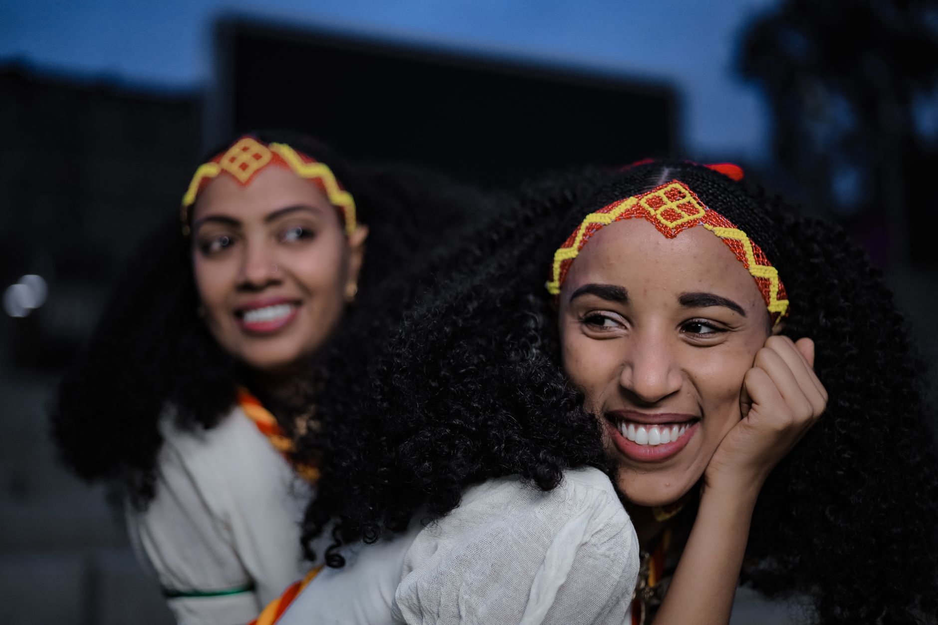 Two smiling women in traditional Ethiopian clothing and headbands, outdoors in Addis