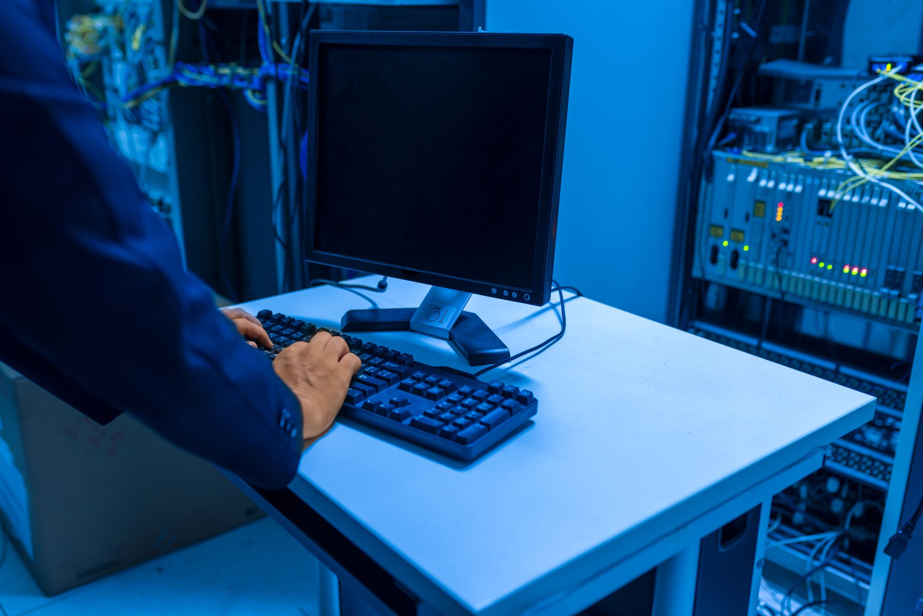 An IT professional operates a computer in a server room, managing network
