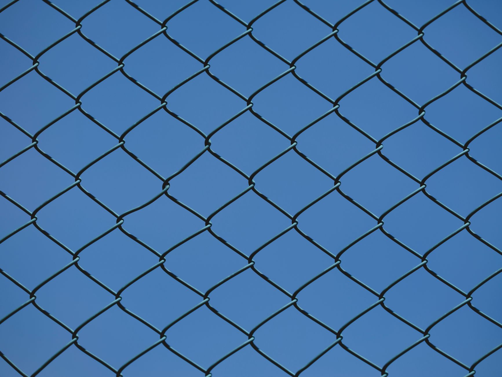 Close-up of a metal chain link fence with clear blue sky in
