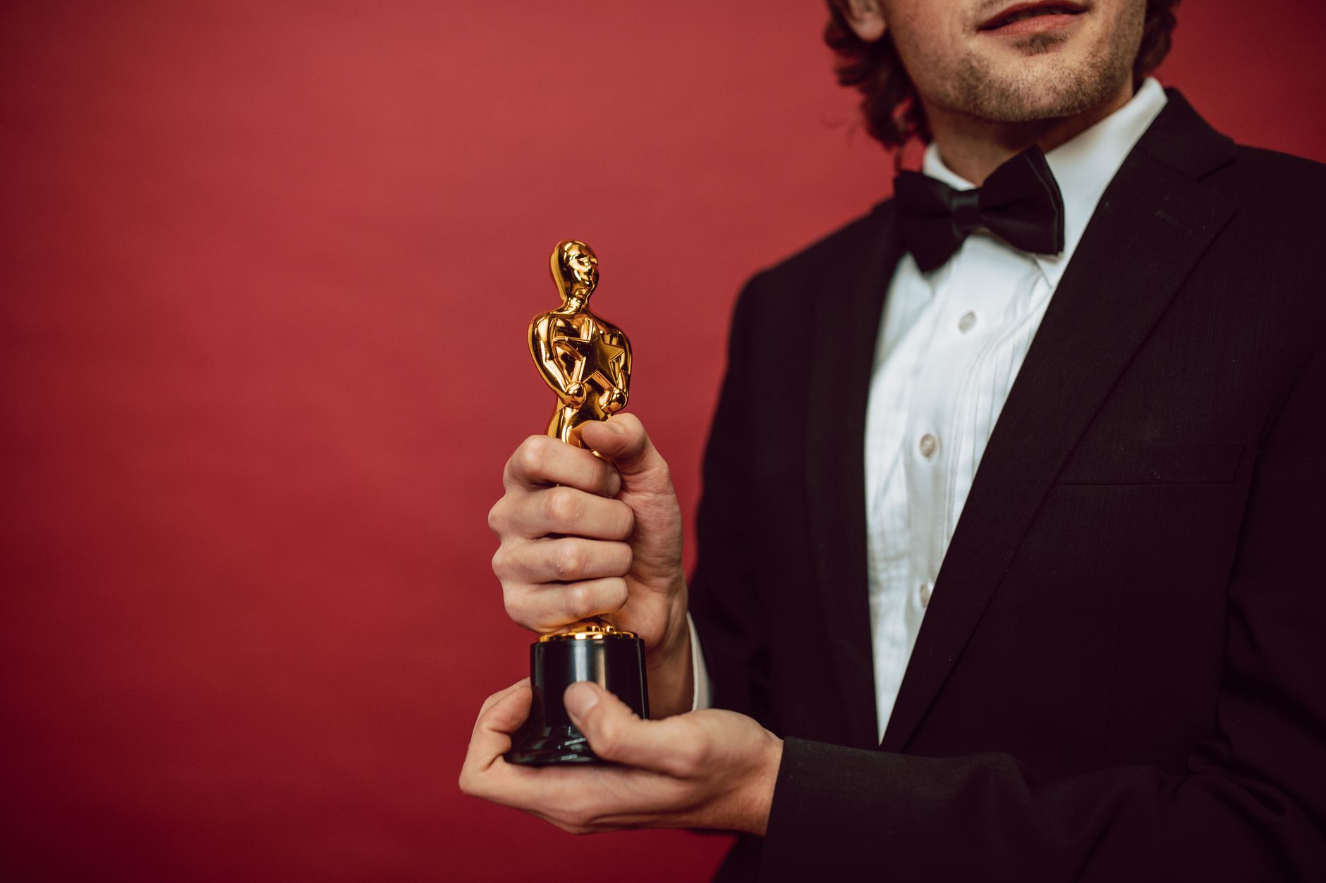 Elegant man in tuxedo holding a gold trophy against a red background,
