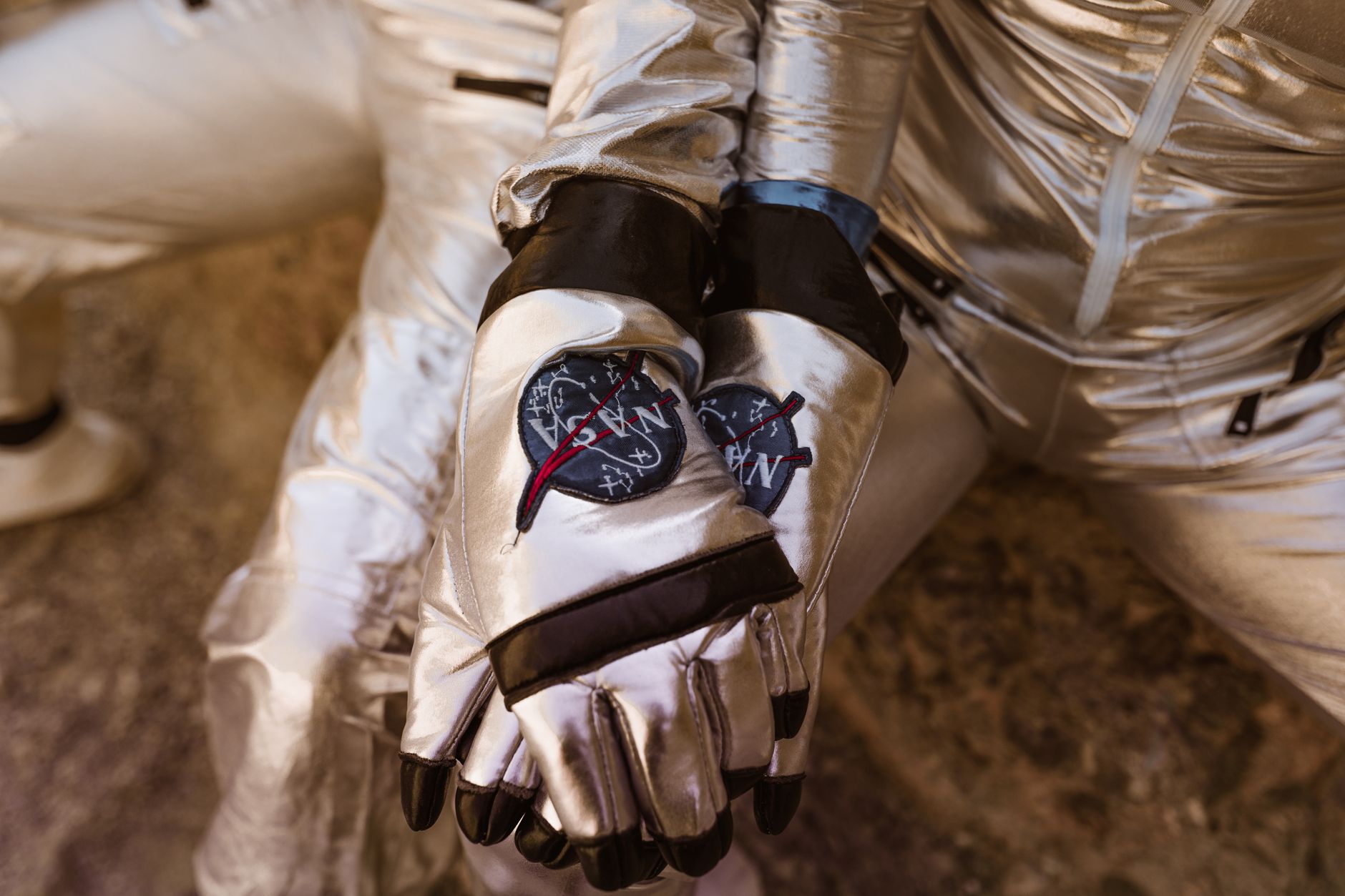 A close-up of two astronauts wearing silver space suits, holding hands, reflecting sci-fi themes.
