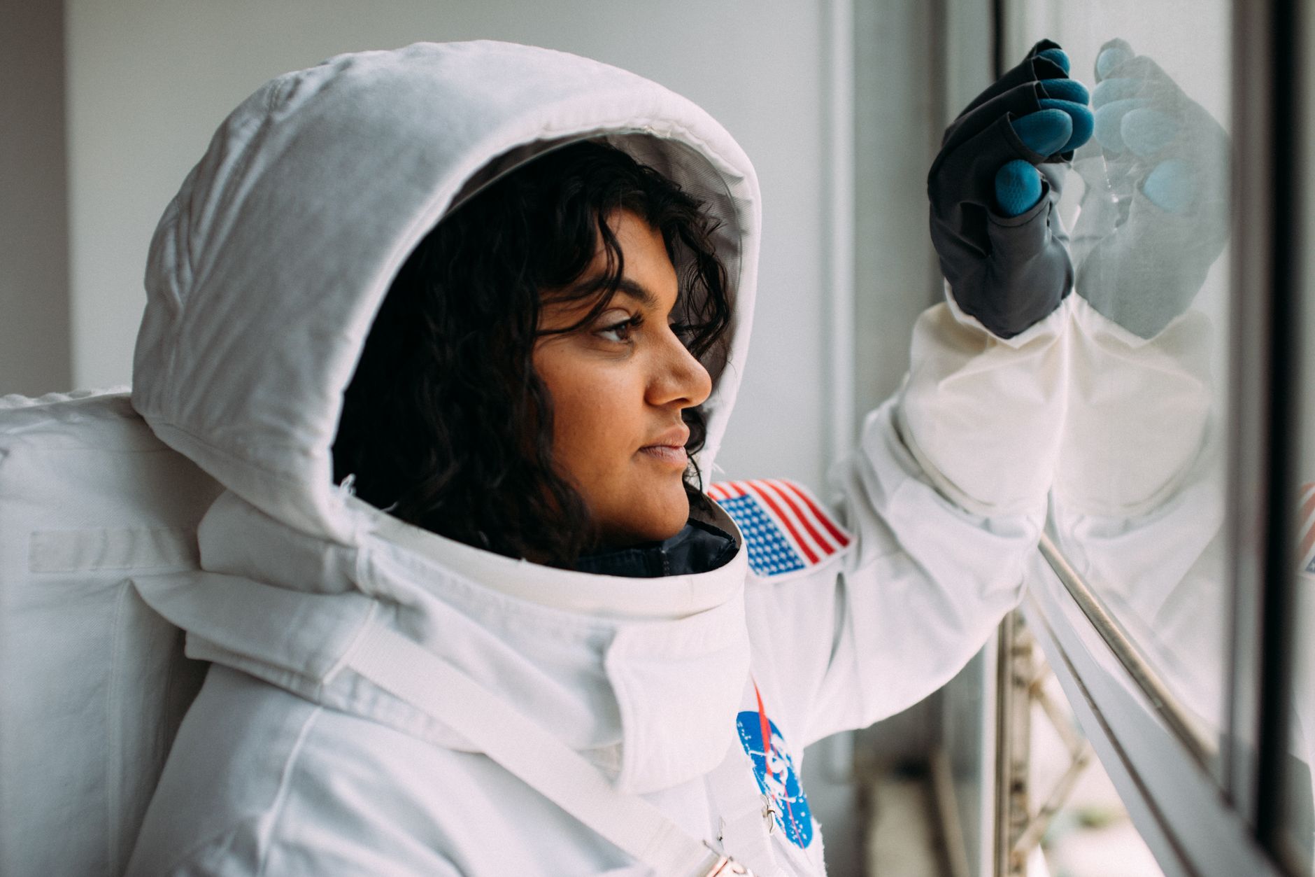 A woman in an astronaut suit looks thoughtfully out of a window,
