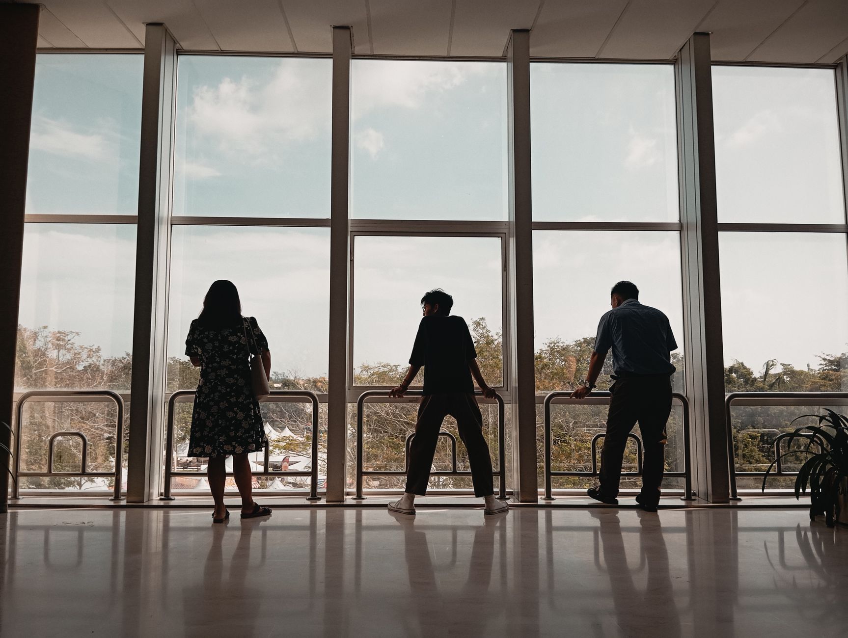 Three people standing by large windows in a modern building lobby with