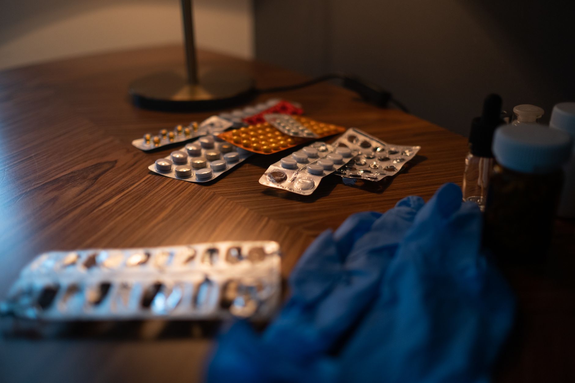 Close-up of various medication blister packs and gloves on a wooden table,
