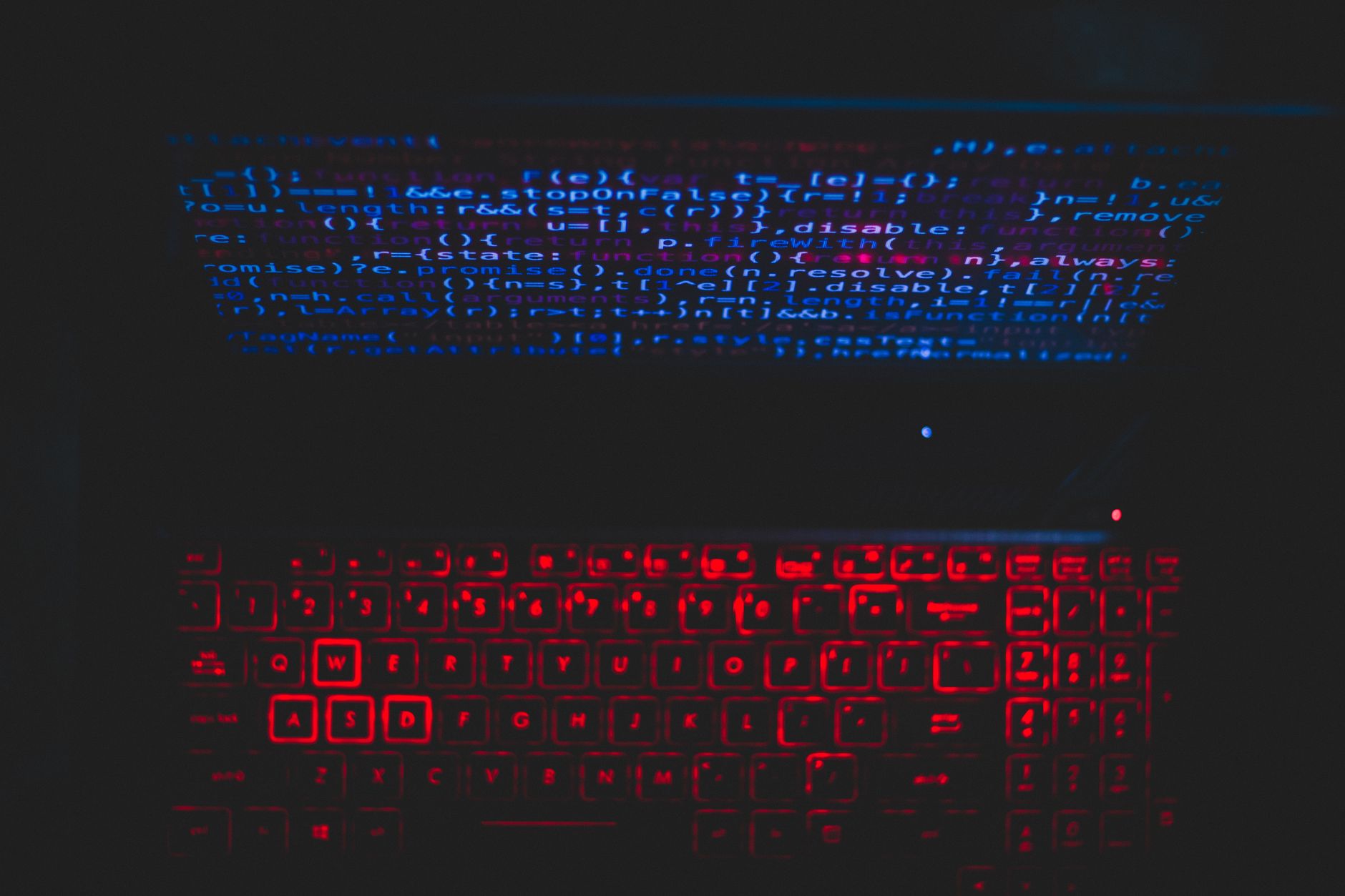 Dark-themed laptop setup with a red glowing keyboard and code on screen,