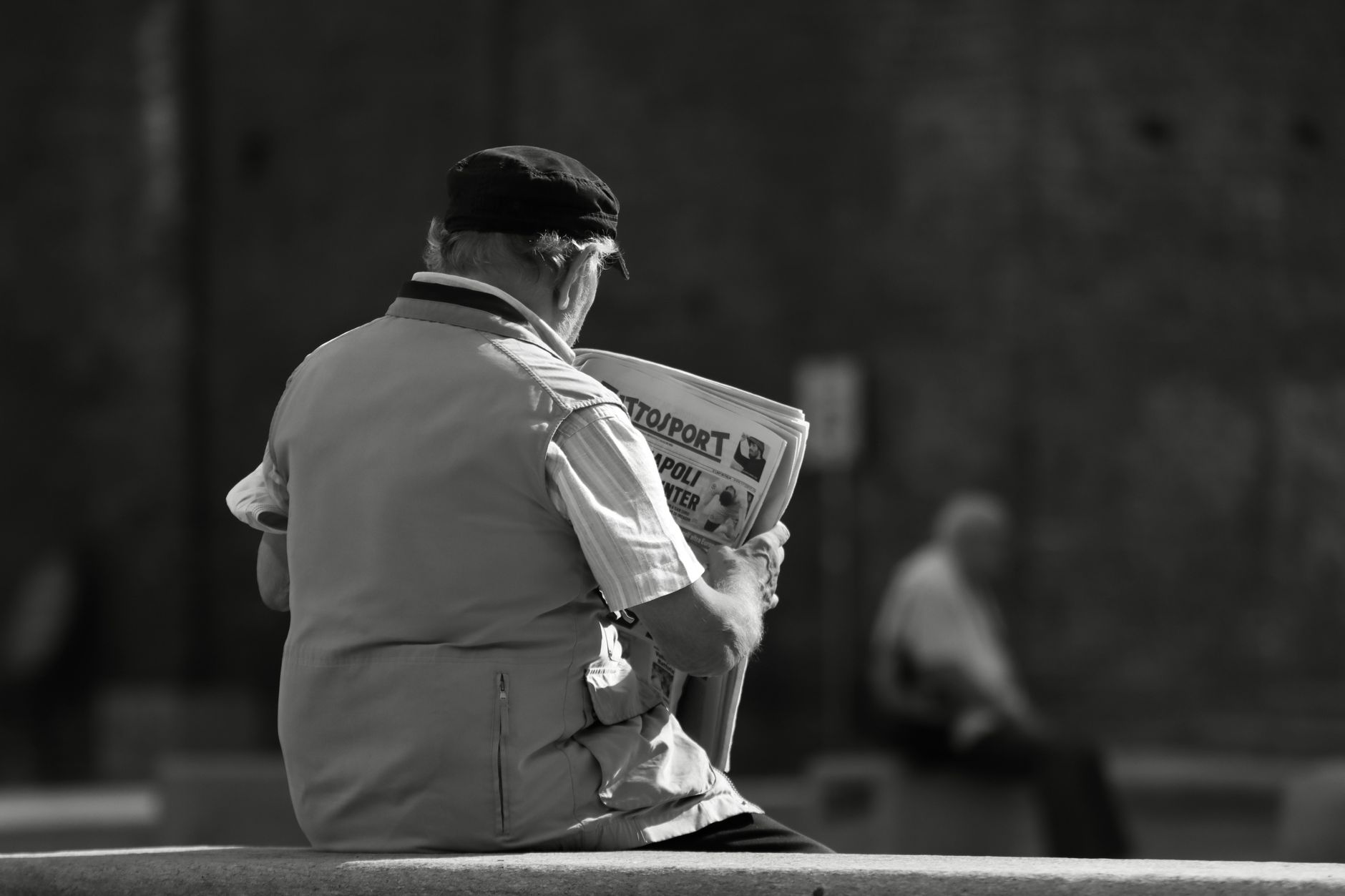 Black and white image of an elderly man reading a newspaper outdoors in Turin, Italy.