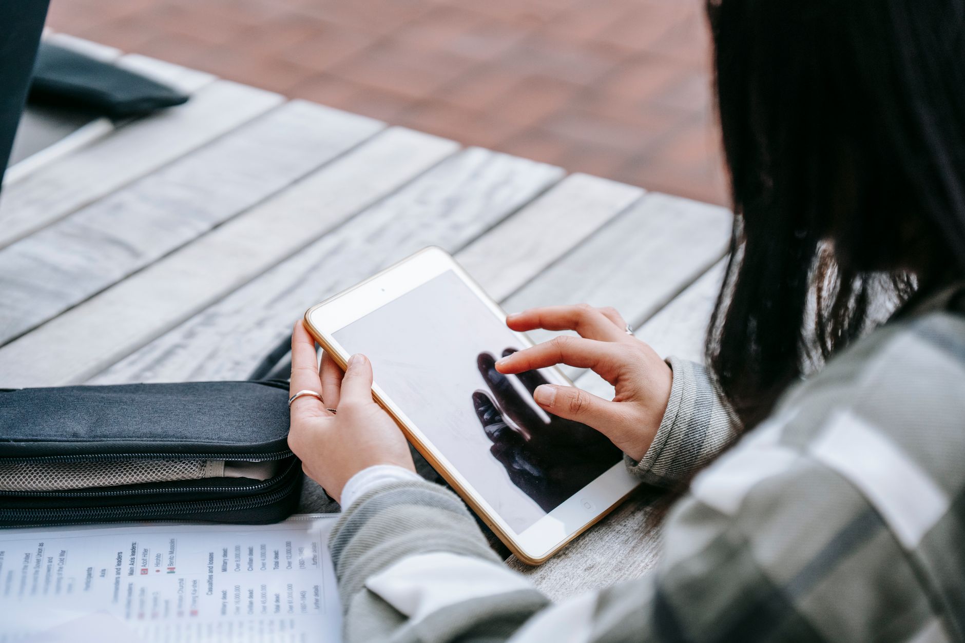 High angle of crop anonymous female student using tablet sitting at wooden