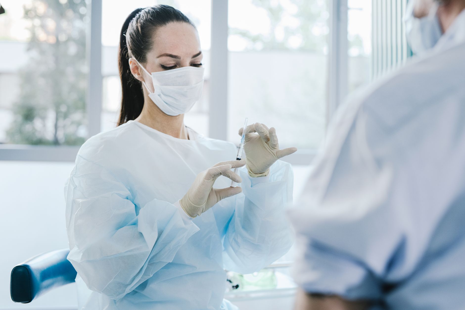 Female doctor in protective gear preparing a syringe in a medical setting.