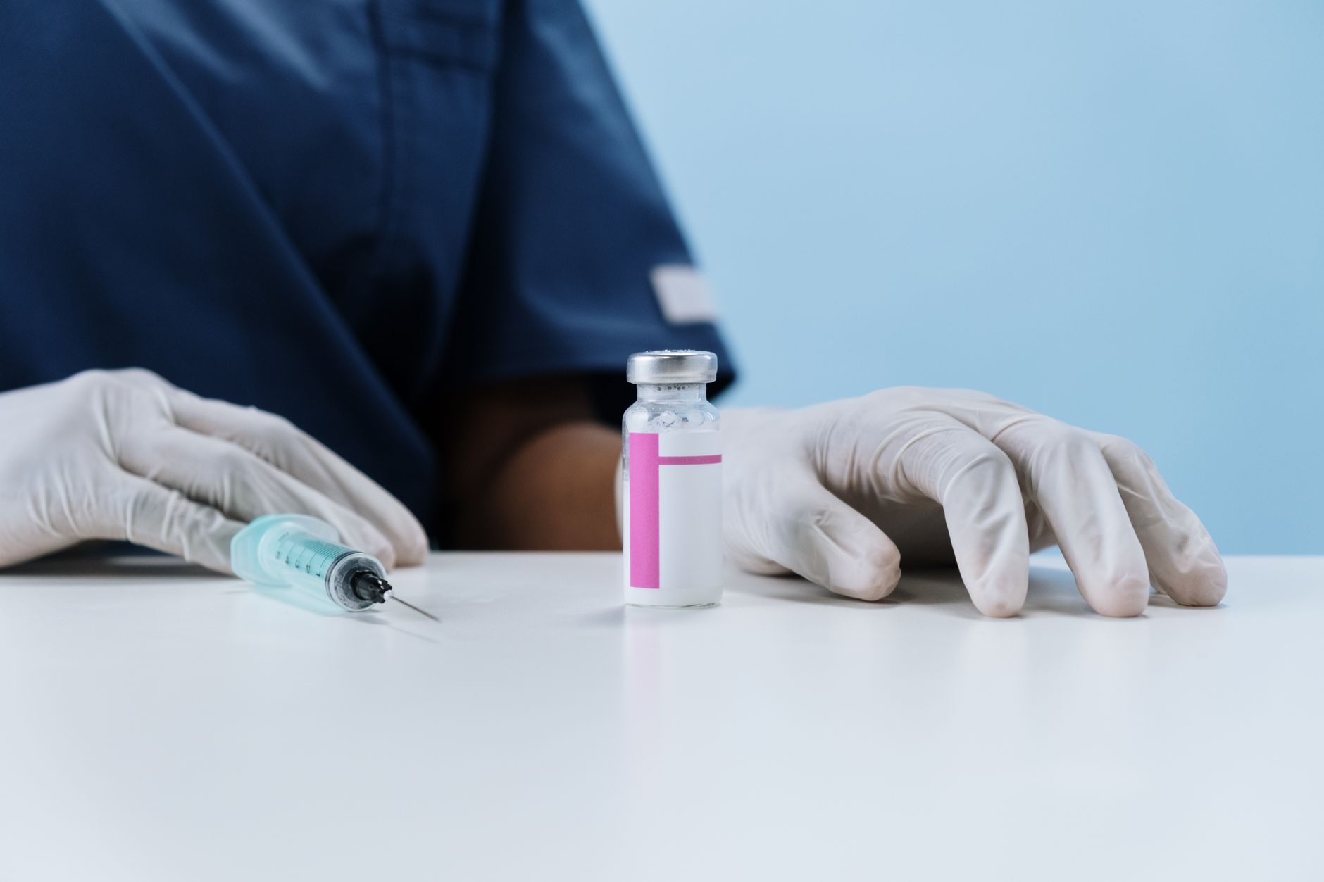 Close-up of healthcare worker's gloved hands with syringe and vaccine vial on