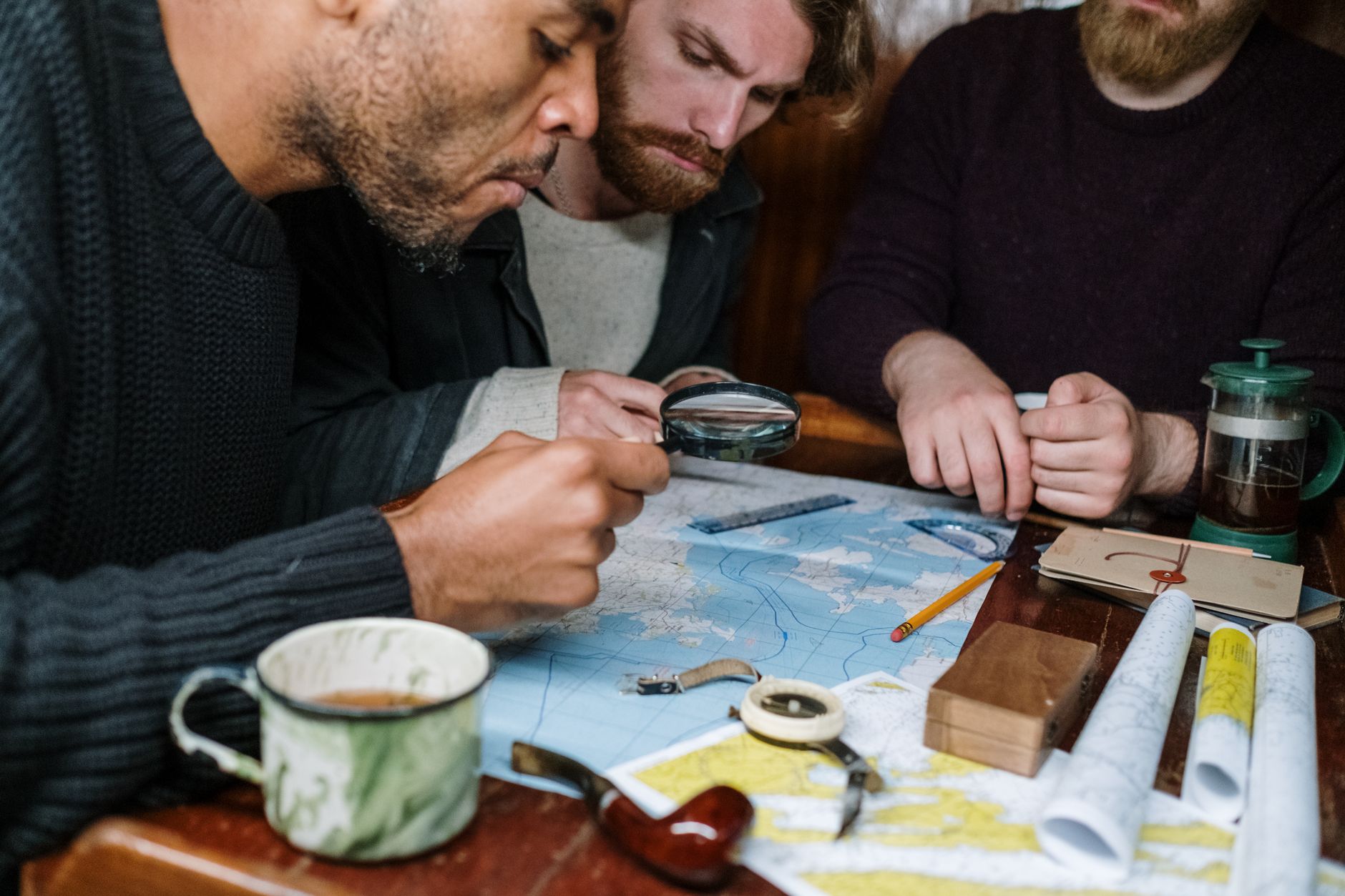 Three men are intensely discussing plans using maps and a magnifying glass,