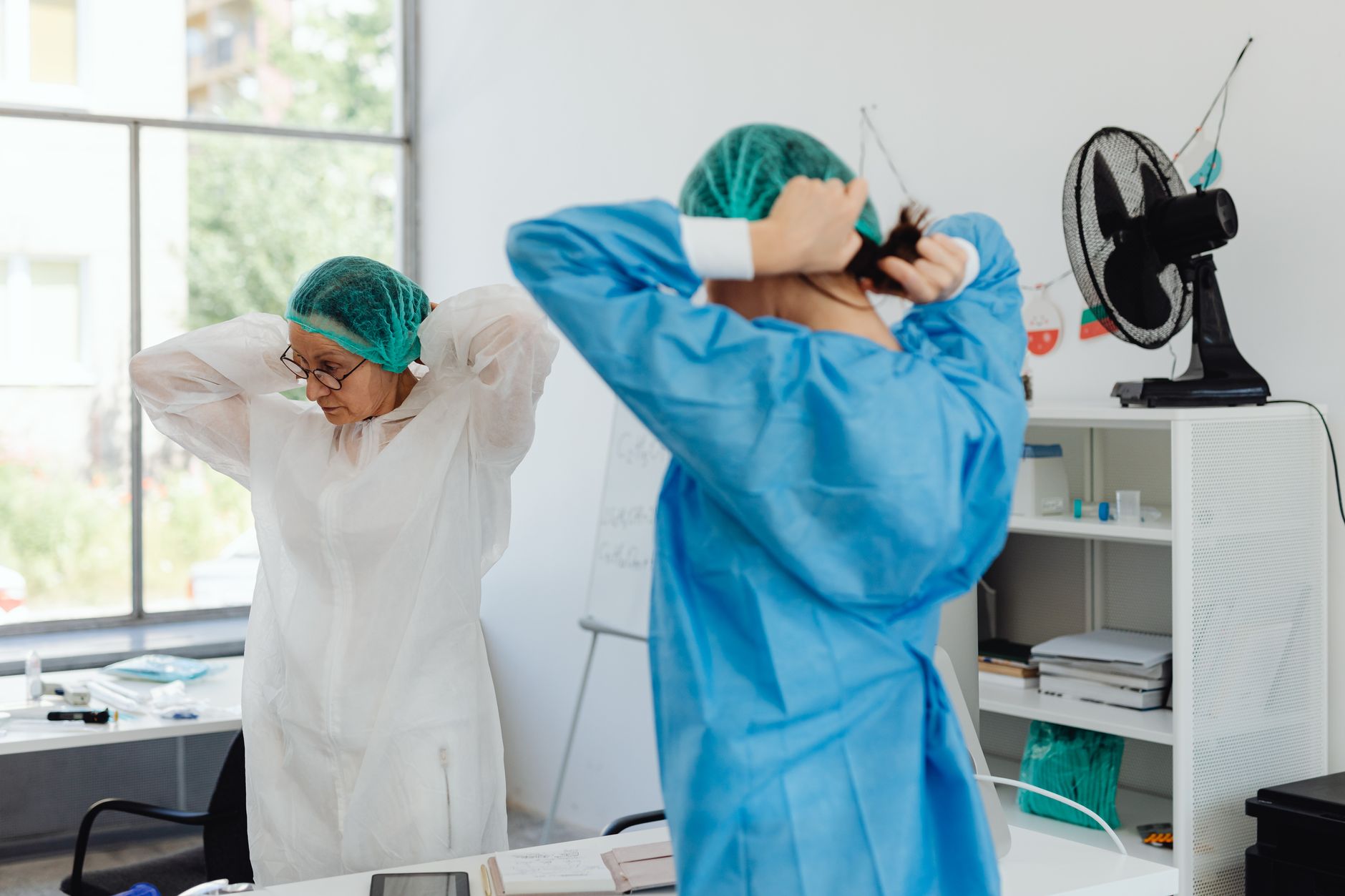 Two healthcare workers in scrubs and hair nets getting ready in a