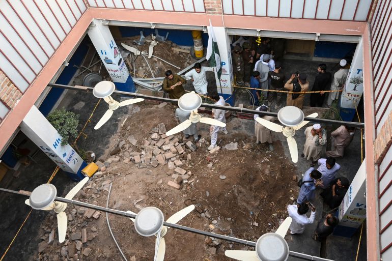 People gather around debris and rubble lying in the courtyard of the Al-Khair Education Centre following a roof collapse, in Peshawar, Pakistan on Thursday
