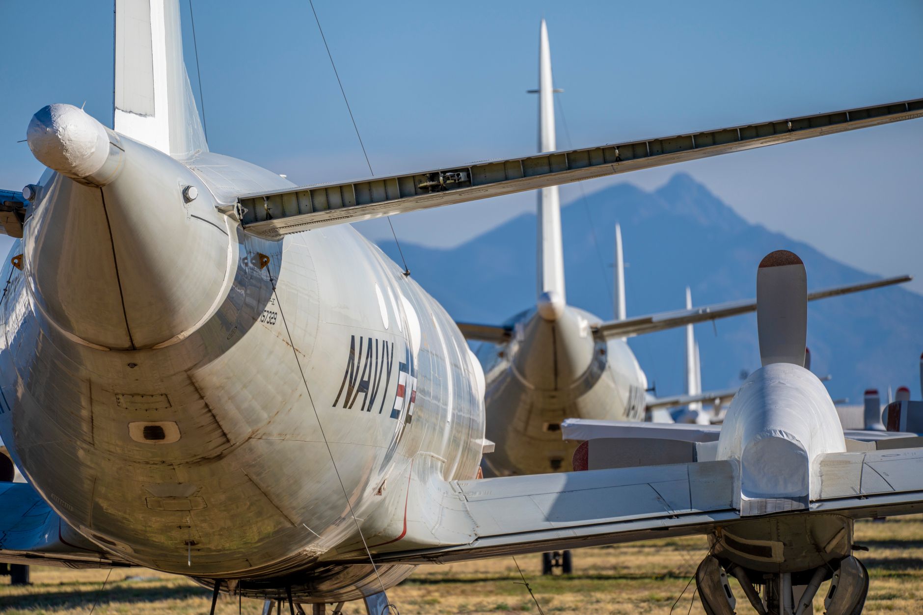 Navy aircraft lined up in the desert with mountains in the distance.