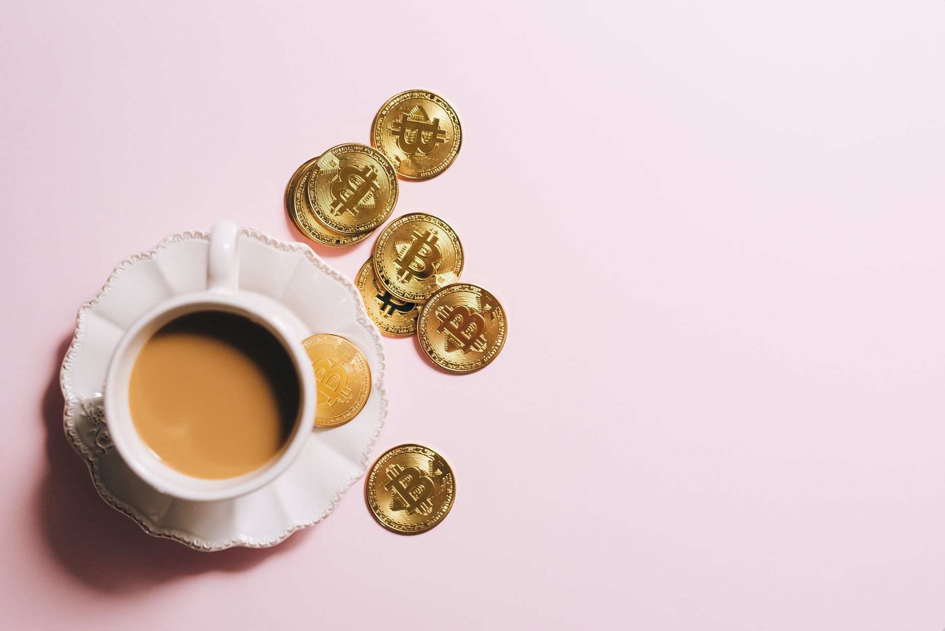 A cup of coffee with Bitcoin gold coins spread across a pastel
