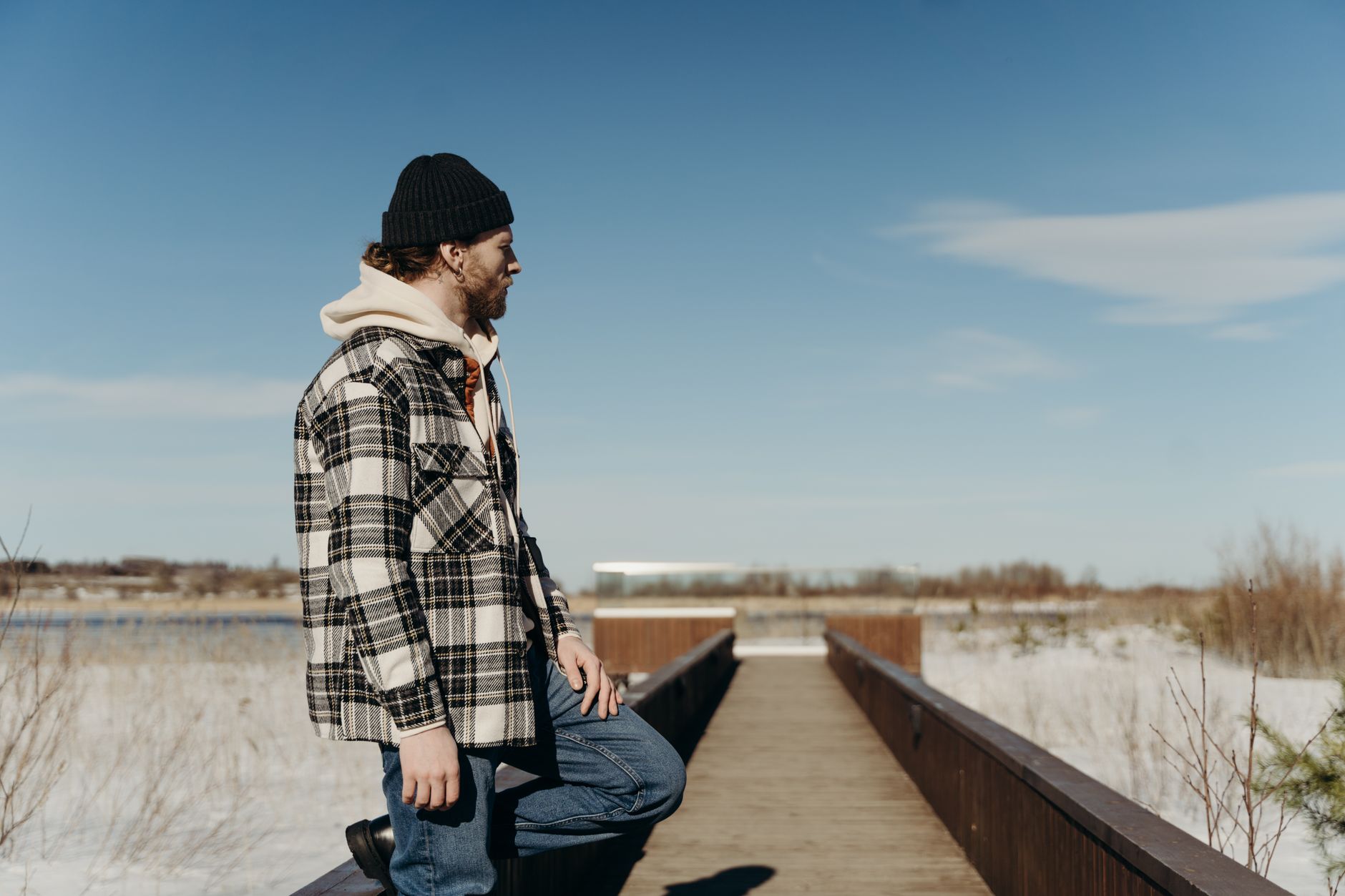 A young man wearing a checkered jacket and knit cap stands on