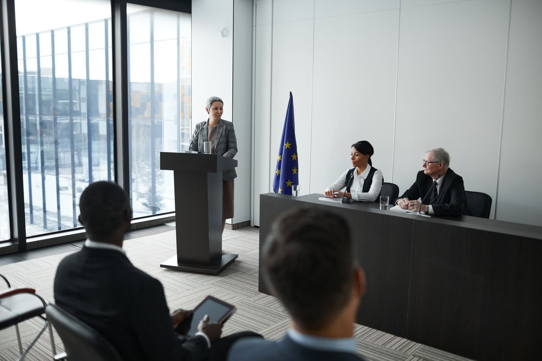 Professional conference setting with a speaker at a podium and attentive audience in a modern meeting room.