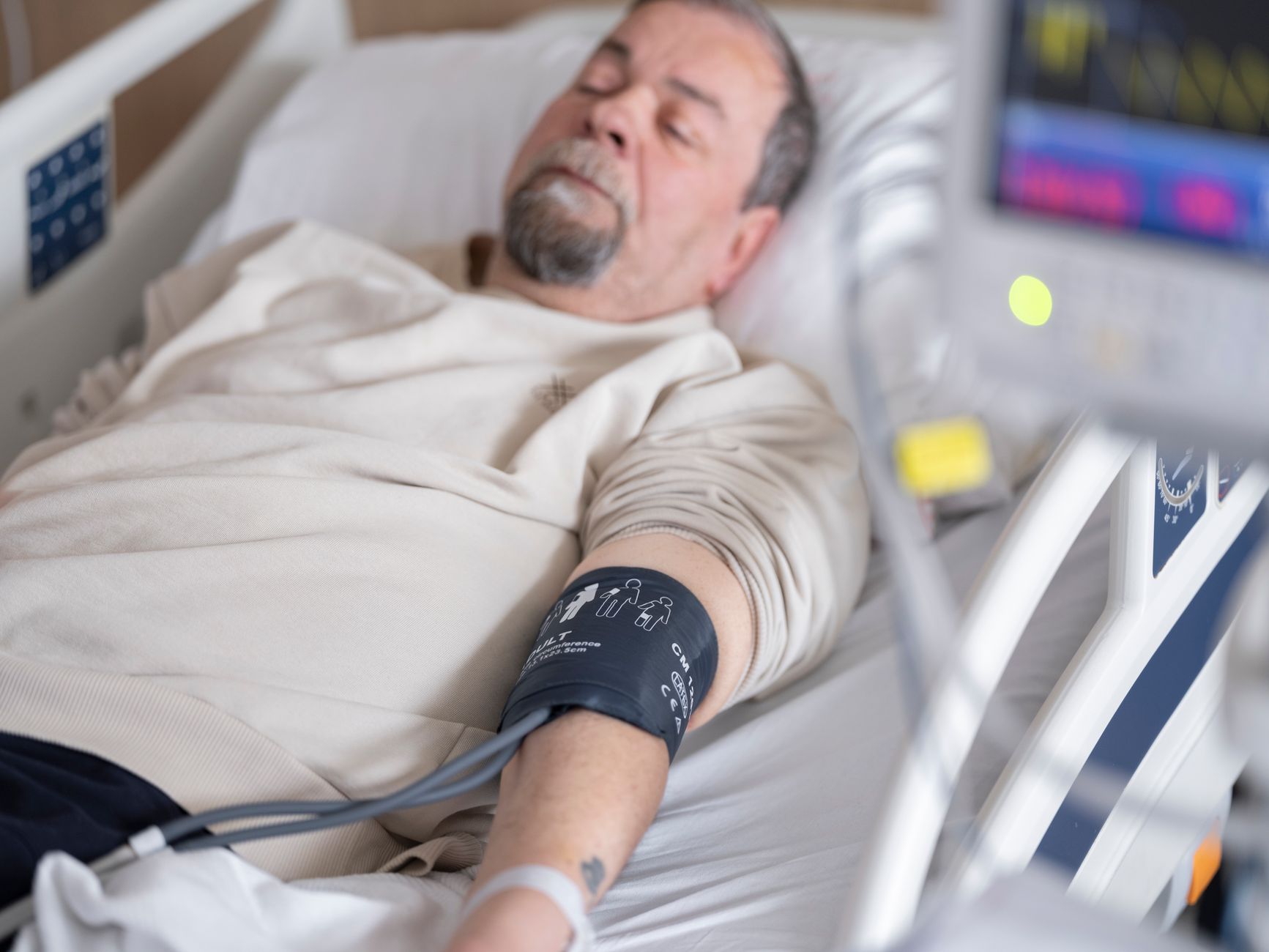 Elderly man resting in hospital bed with blood pressure monitor attached, symbolizing