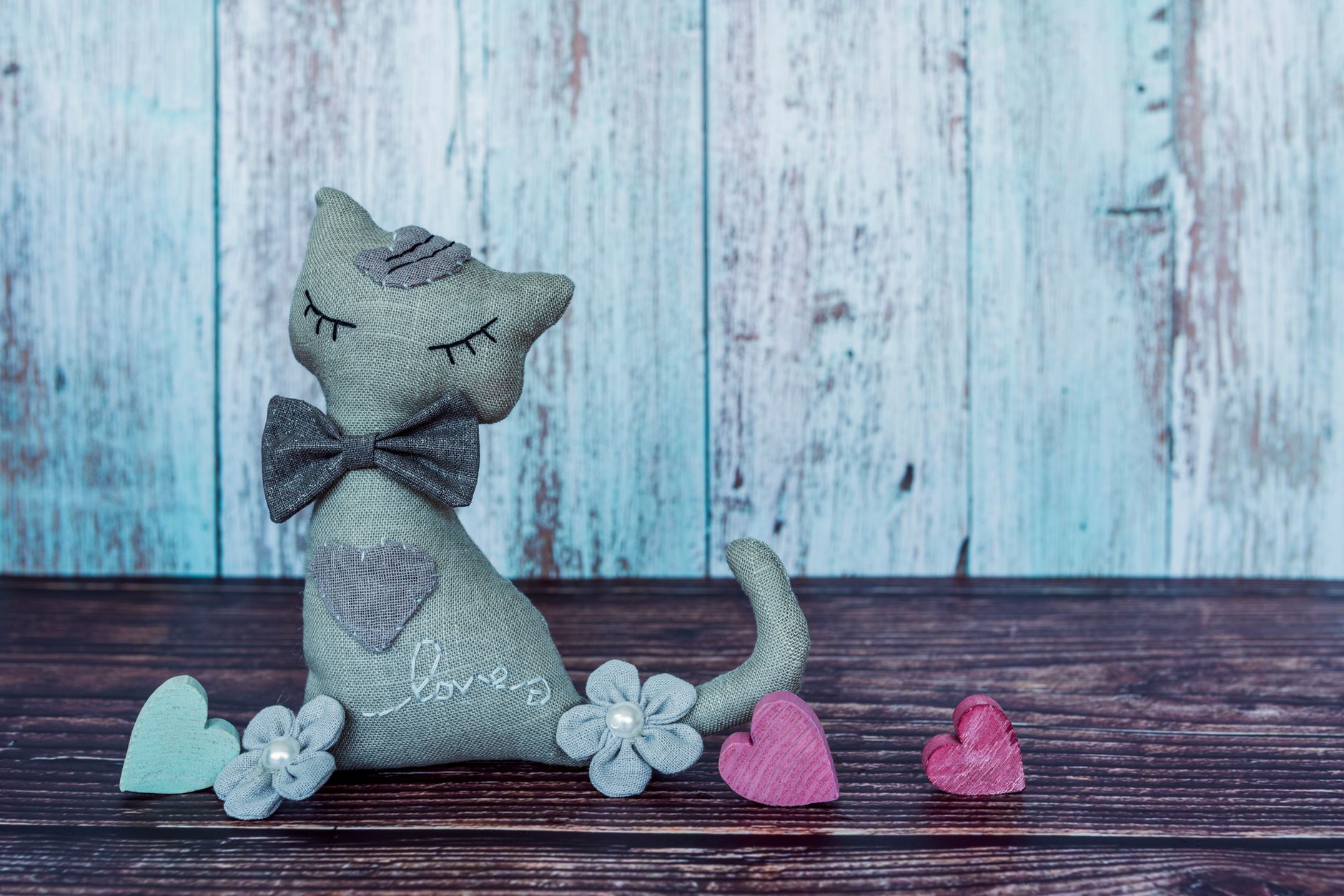 Rustic handmade cat plush with colorful hearts and flowers against a wooden