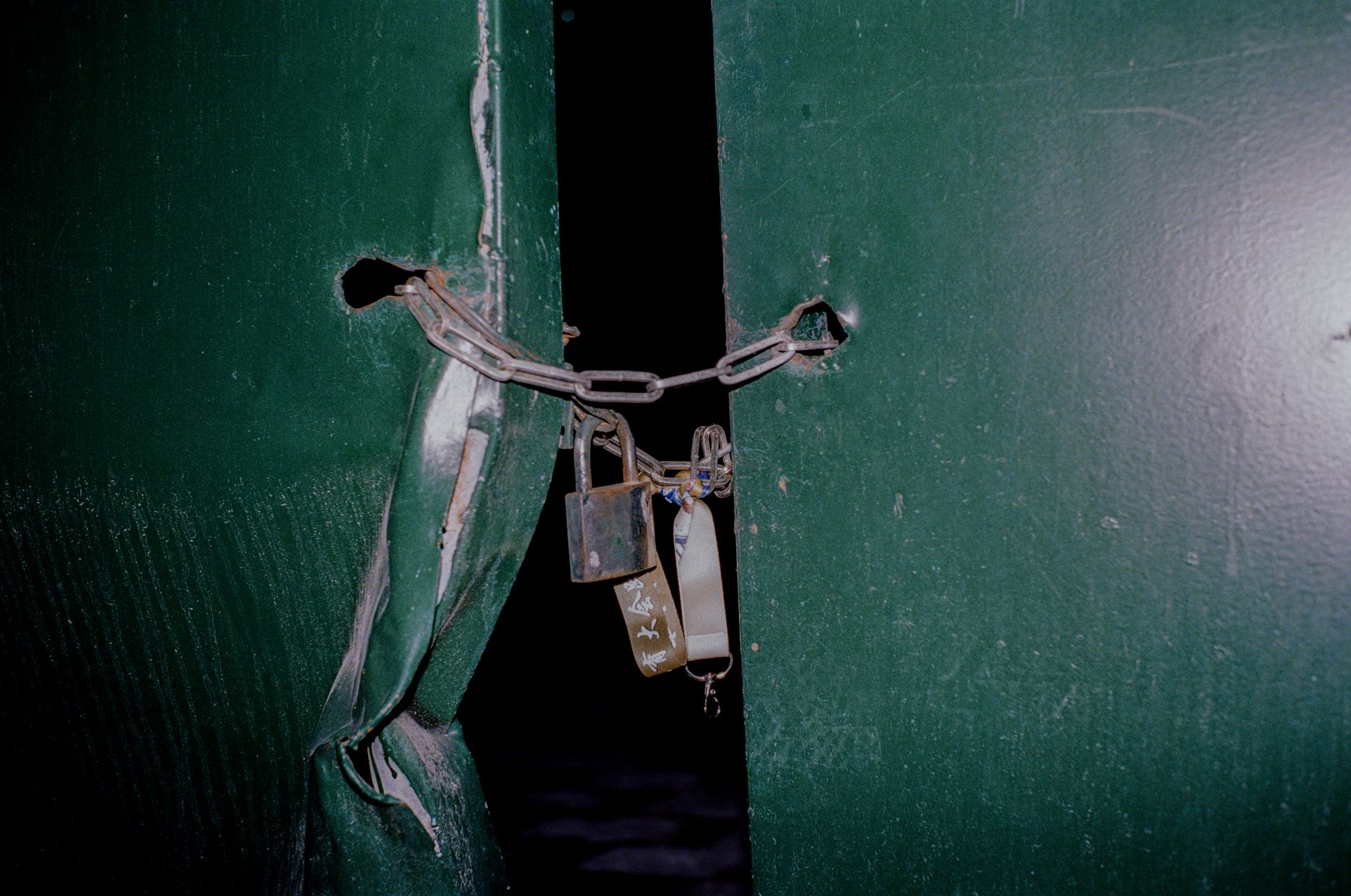 Close-up of a rusty padlock and chain securing green metal doors, blocking