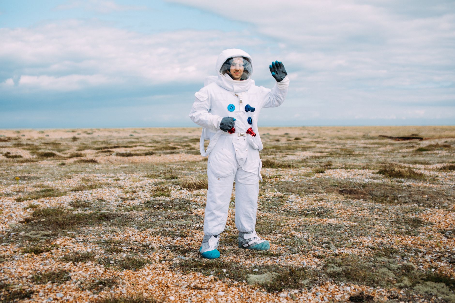 Astronaut in a spacesuit waving in an open desolate landscape under a