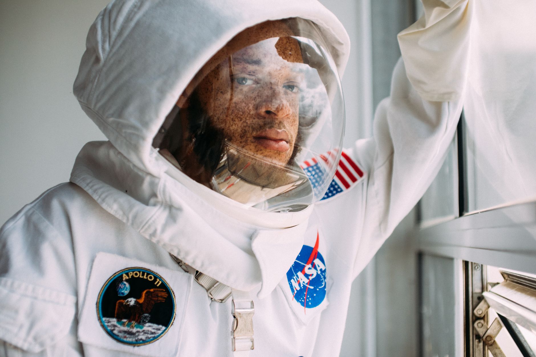 Close-up portrait of an astronaut wearing a NASA space suit looking out a window.