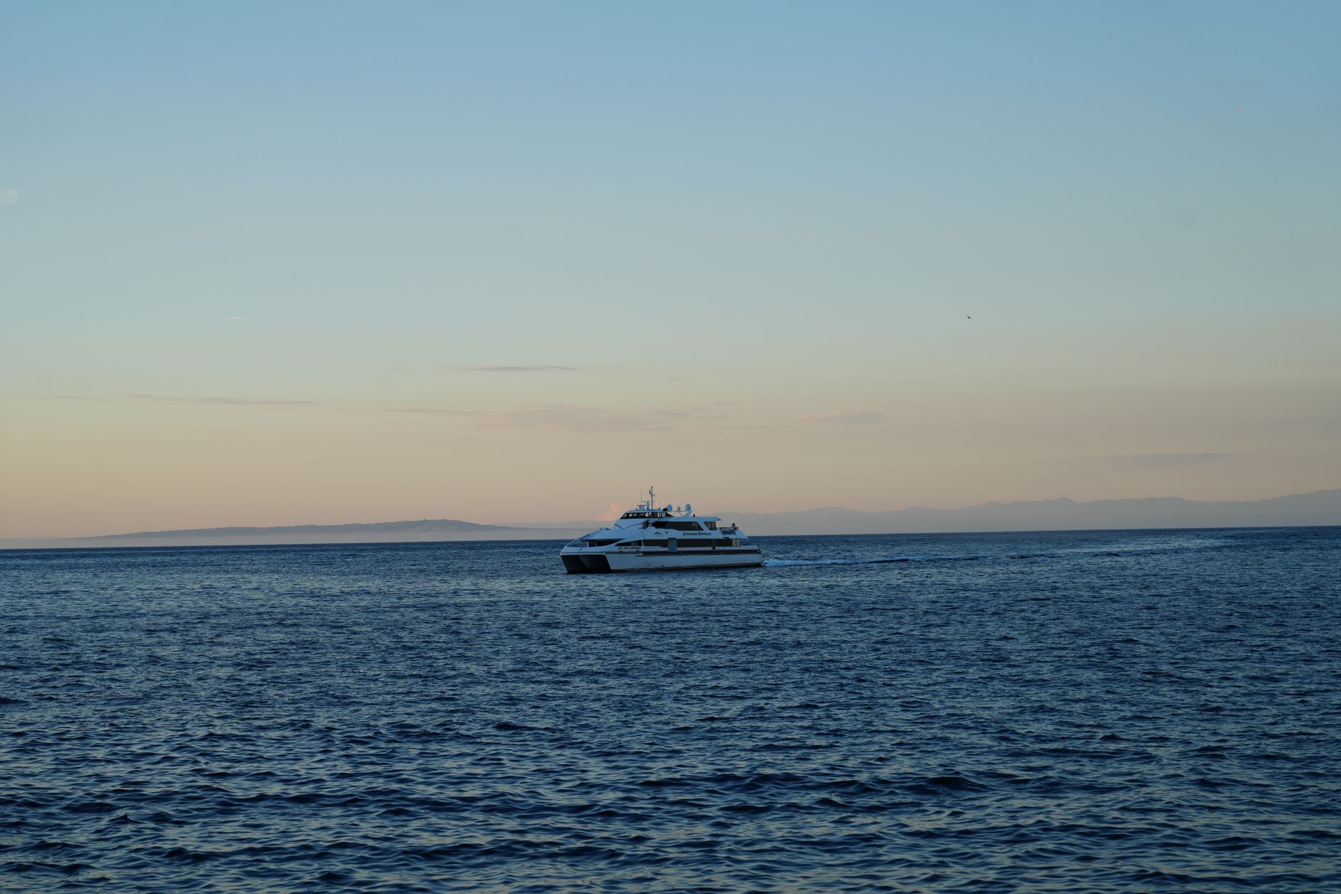 A serene view of a boat sailing on the ocean during sunset with distant land.