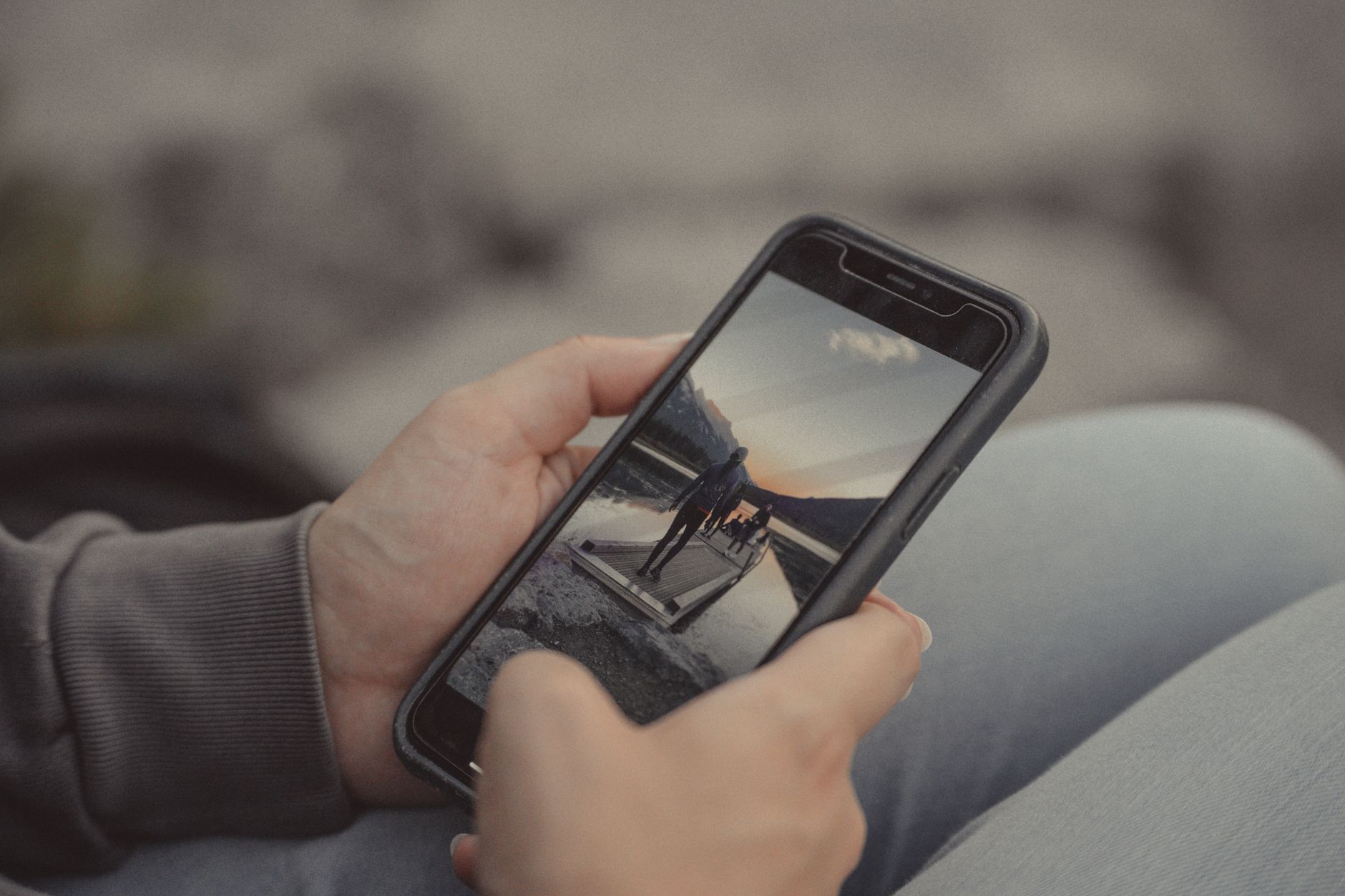 Close-up of hands holding a smartphone showing a mountain scene, captured outdoors