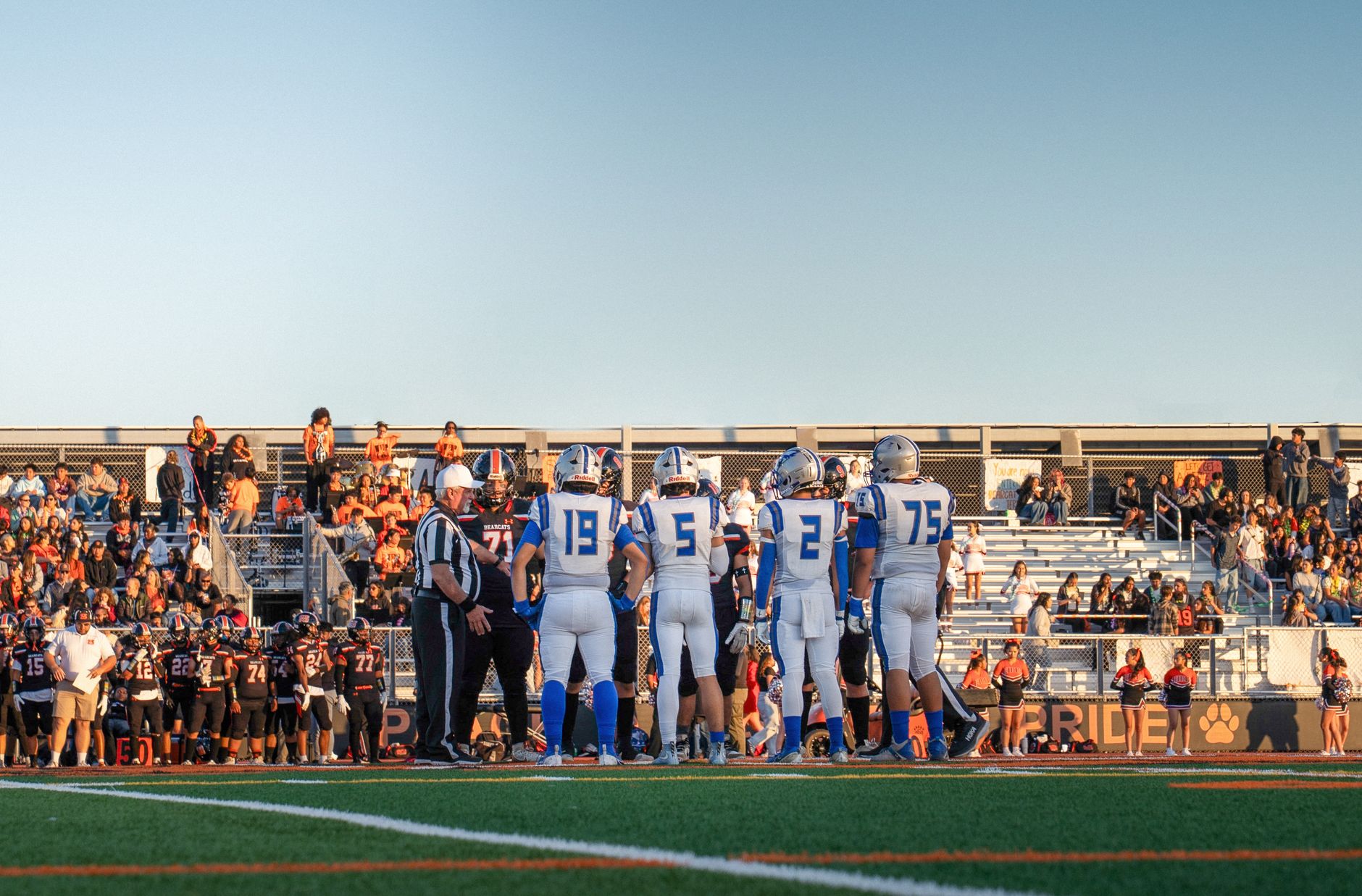 A high school football game during sunset with players and a referee